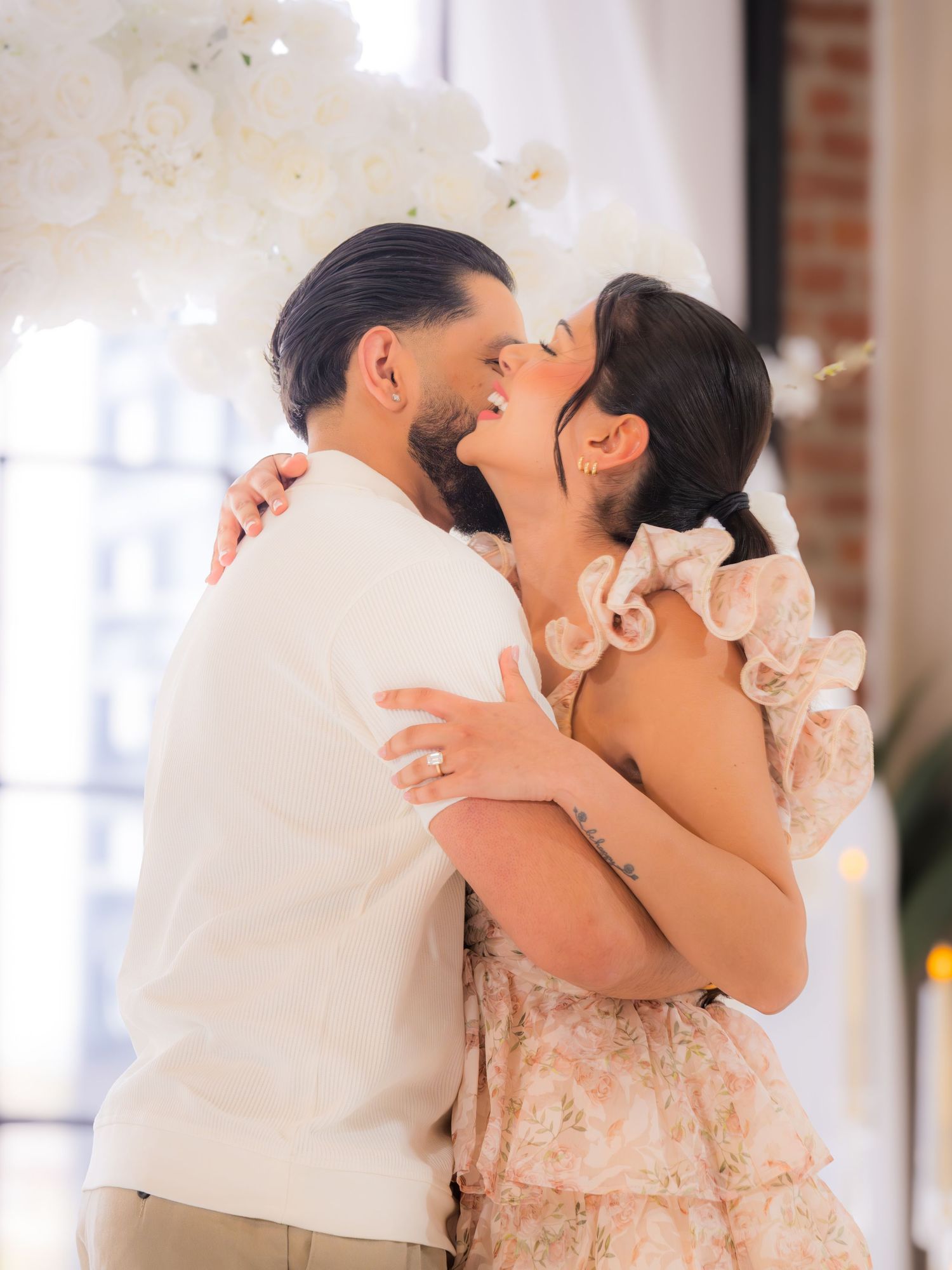 Couple embracing and laughing together at an elegant white floral engagement party venue.