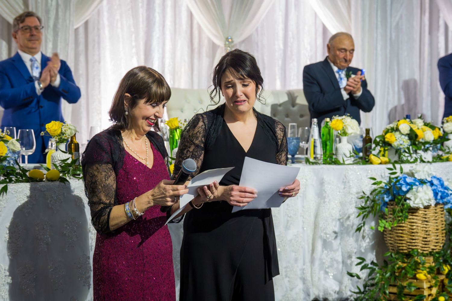 Two women delivering heartfelt speech reading from papers at an elegant anniversary party reception.
