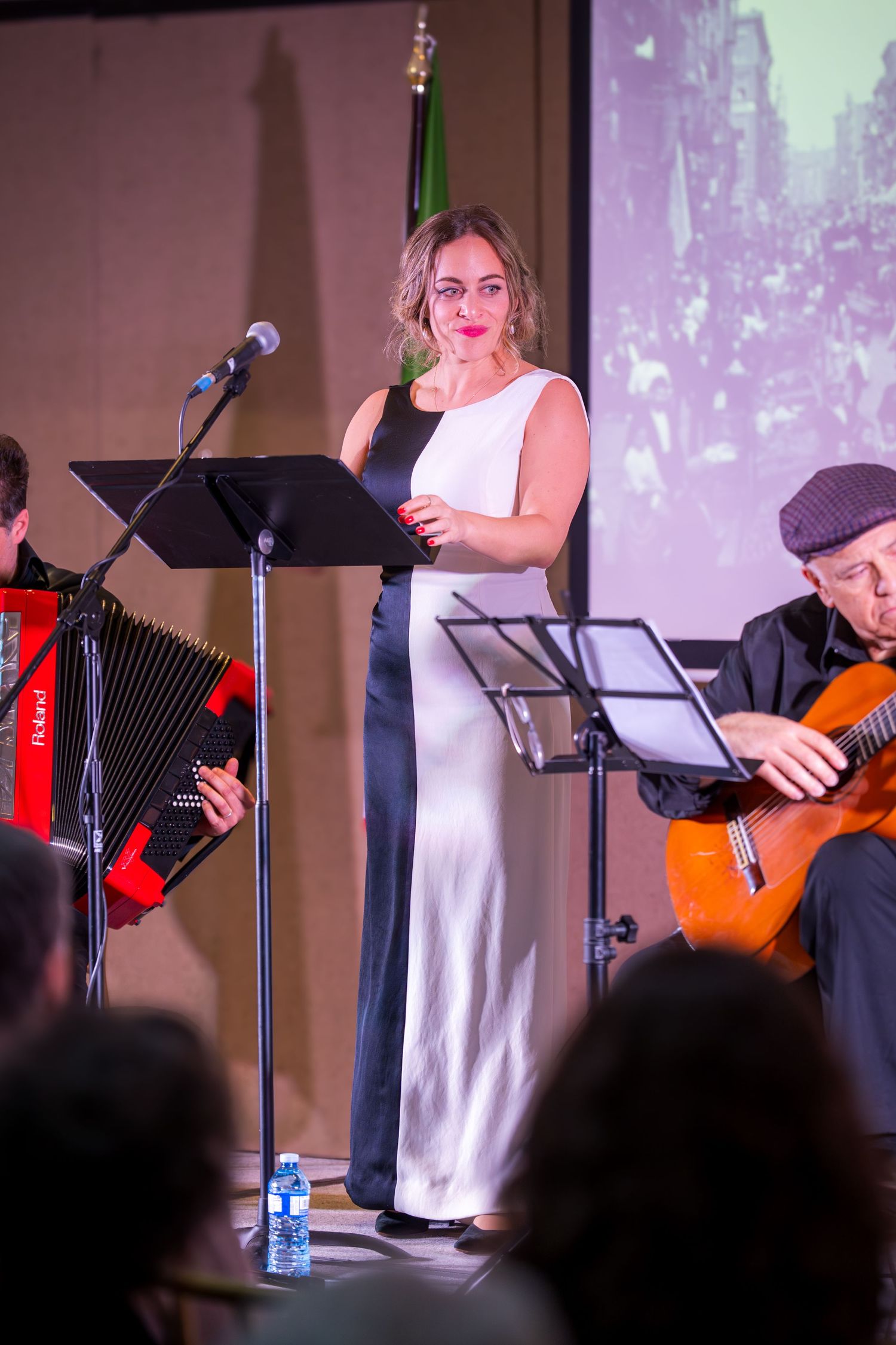 Female vocalist in black and white gown performing with accordion and guitar players on stage.