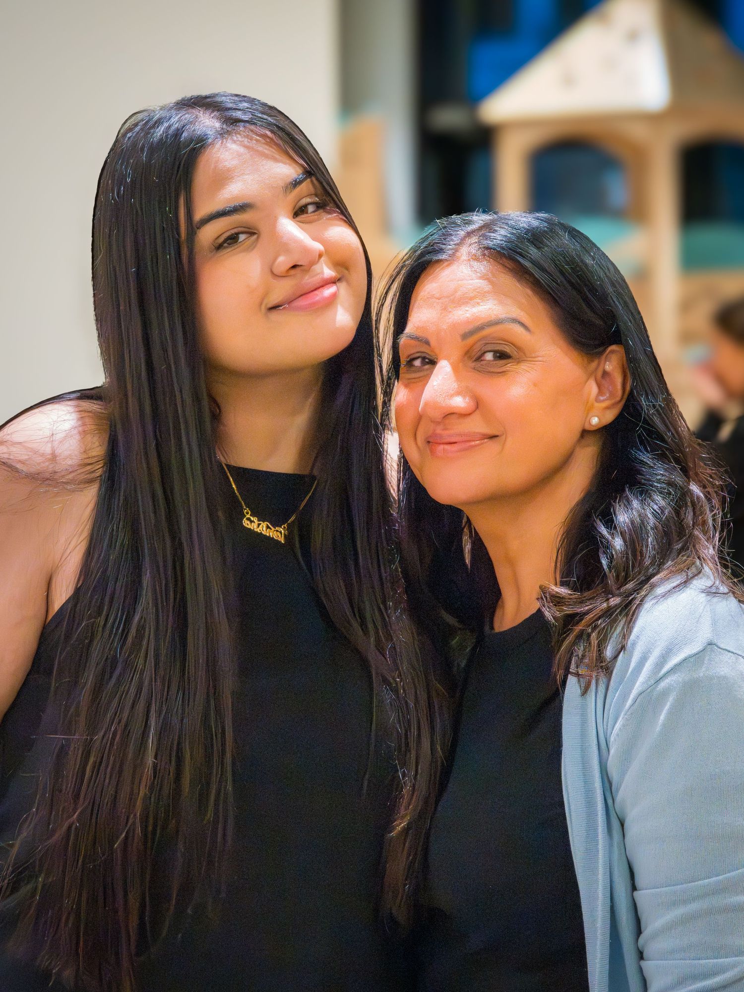 Two women with long dark hair smiling together at an indoor event.