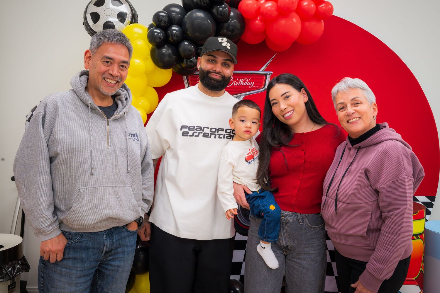 Family of five smiling together at a colorful balloon-decorated birthday celebration.