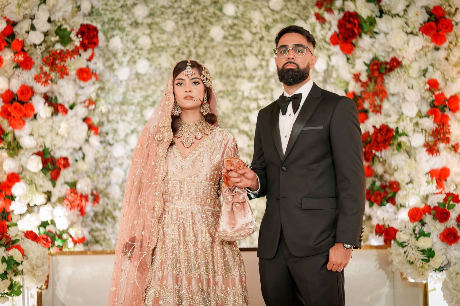 Elegant wedding portraits featuring a floral wall backdrop with red accent flowers.