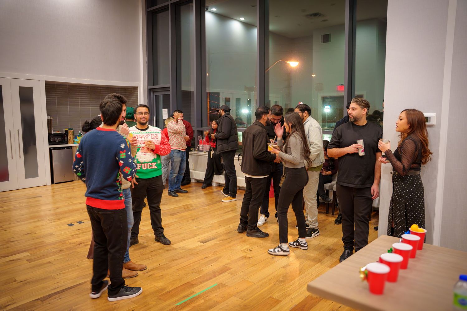 A group mingles at an indoor party with red cups arranged on tables in a modern space.