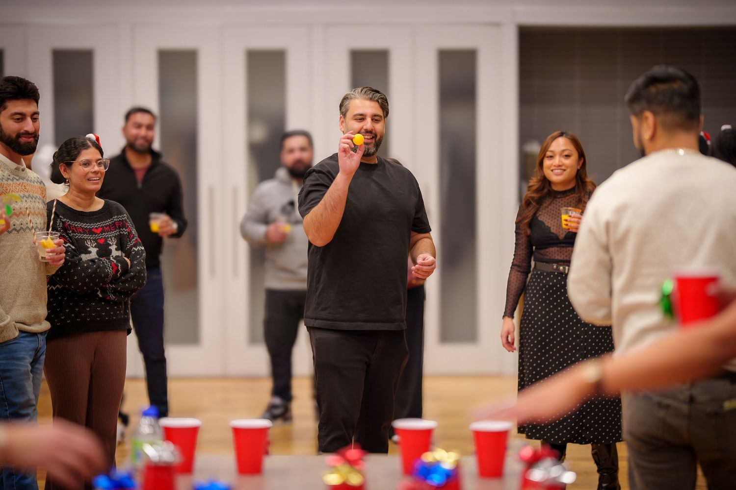 Indoor party scene with people gathered around tables with red cups.