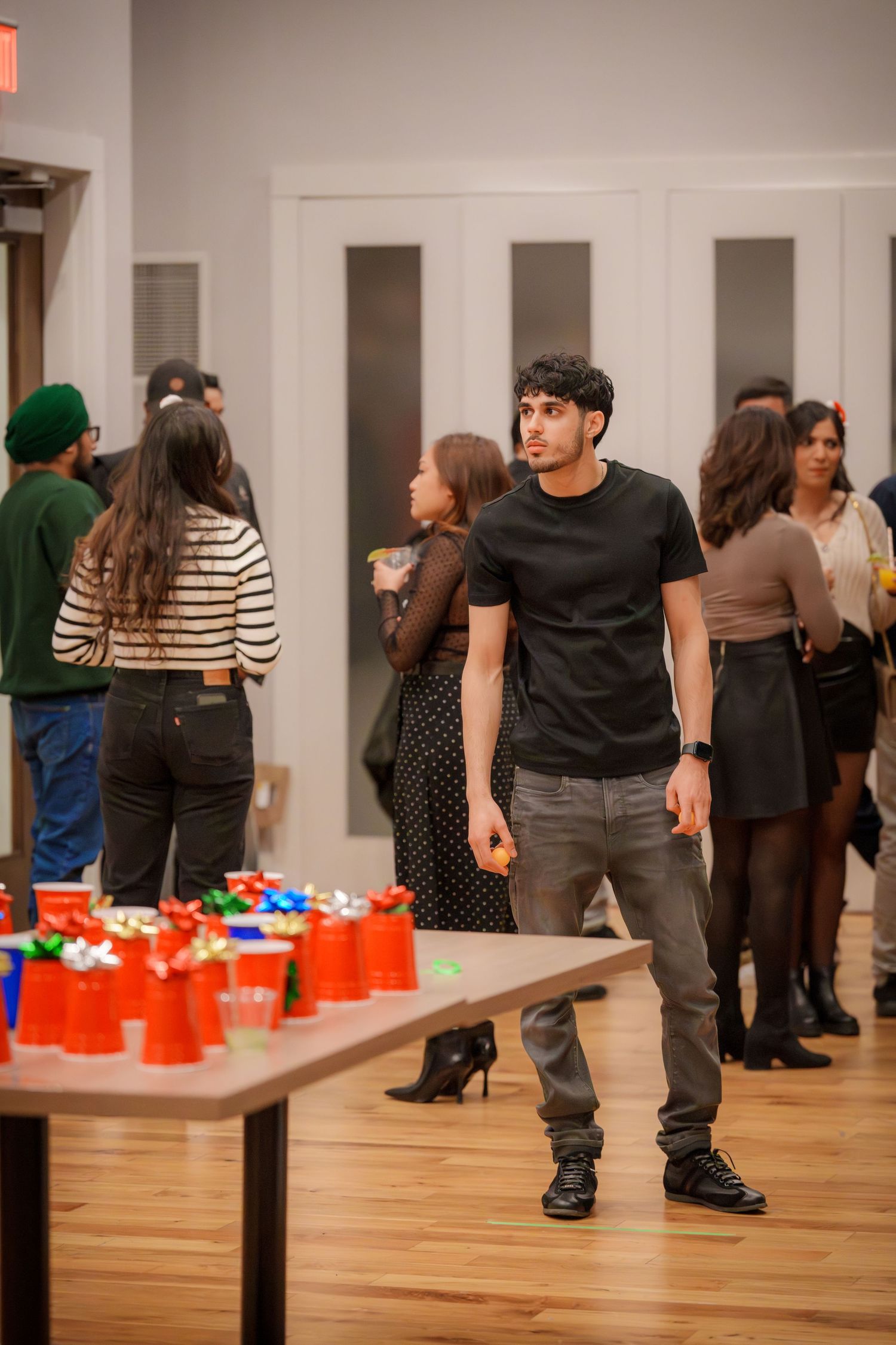 Party guests playing games with red cups on tables in a room with white walls and wooden floors.