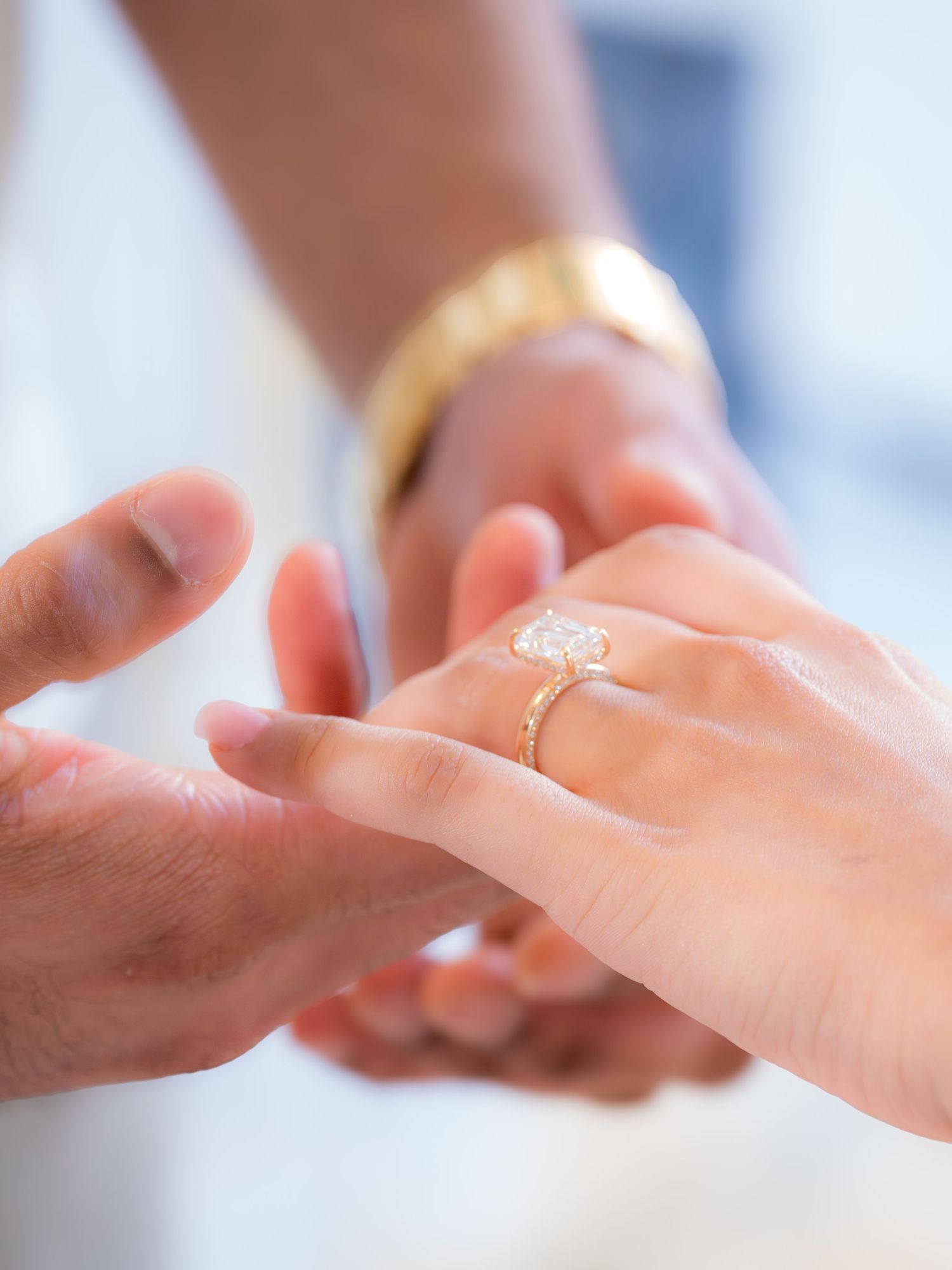 Close-up of man placing diamond solitaire engagement ring on womans finger during proposal.