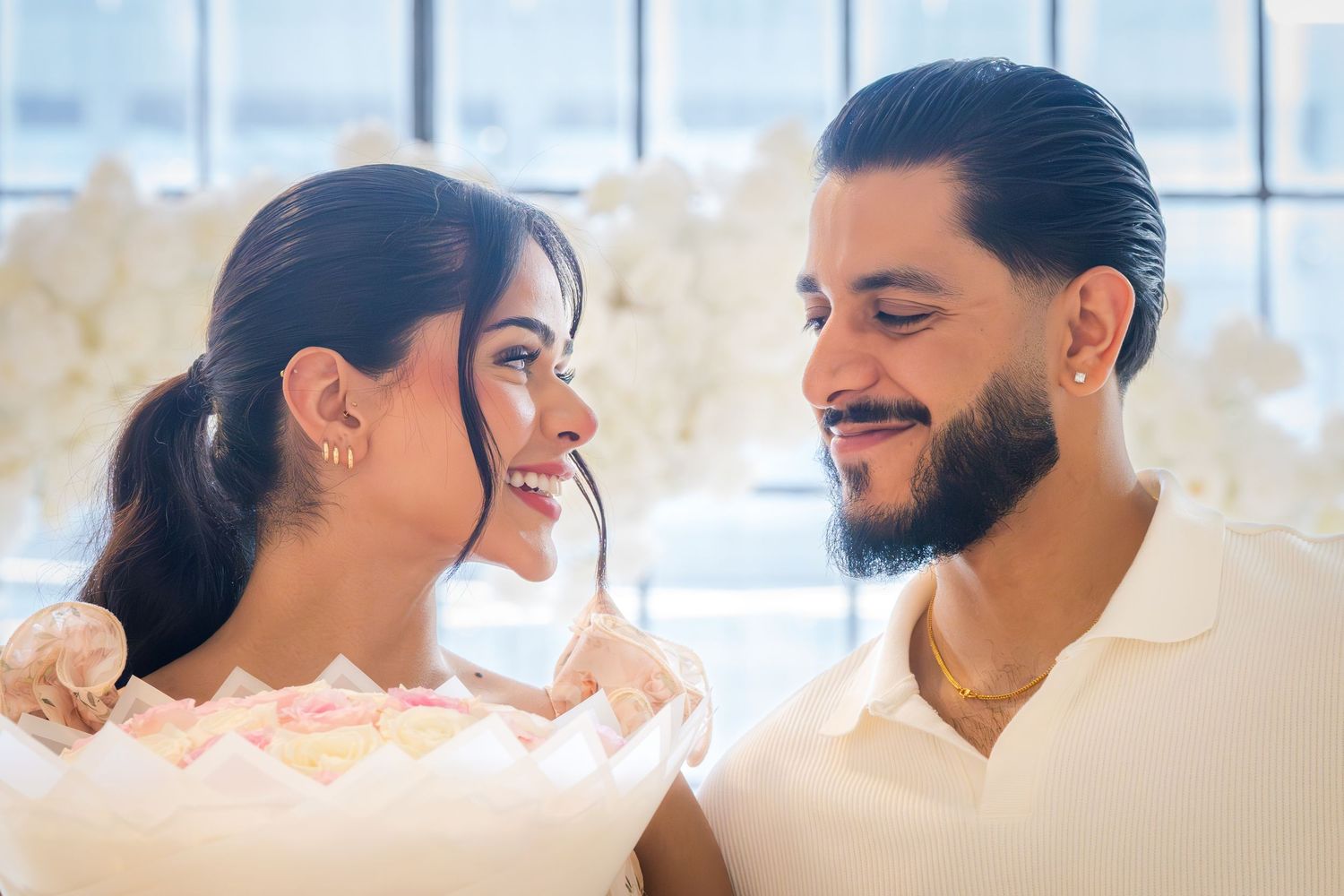 Happy couple smiles at each other while holding a bouquet of flowers after a romantic proposal.