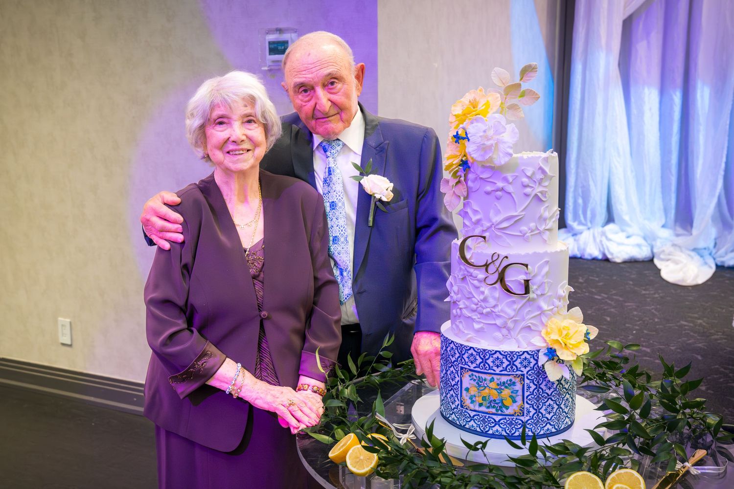 Elderly couple standing together beside a elegant tiered anniversary celebration cake.
