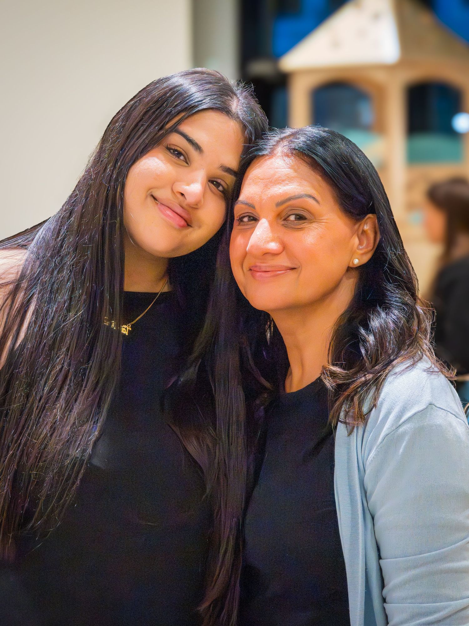 Two women with long dark hair smiling together at an indoor play venue.