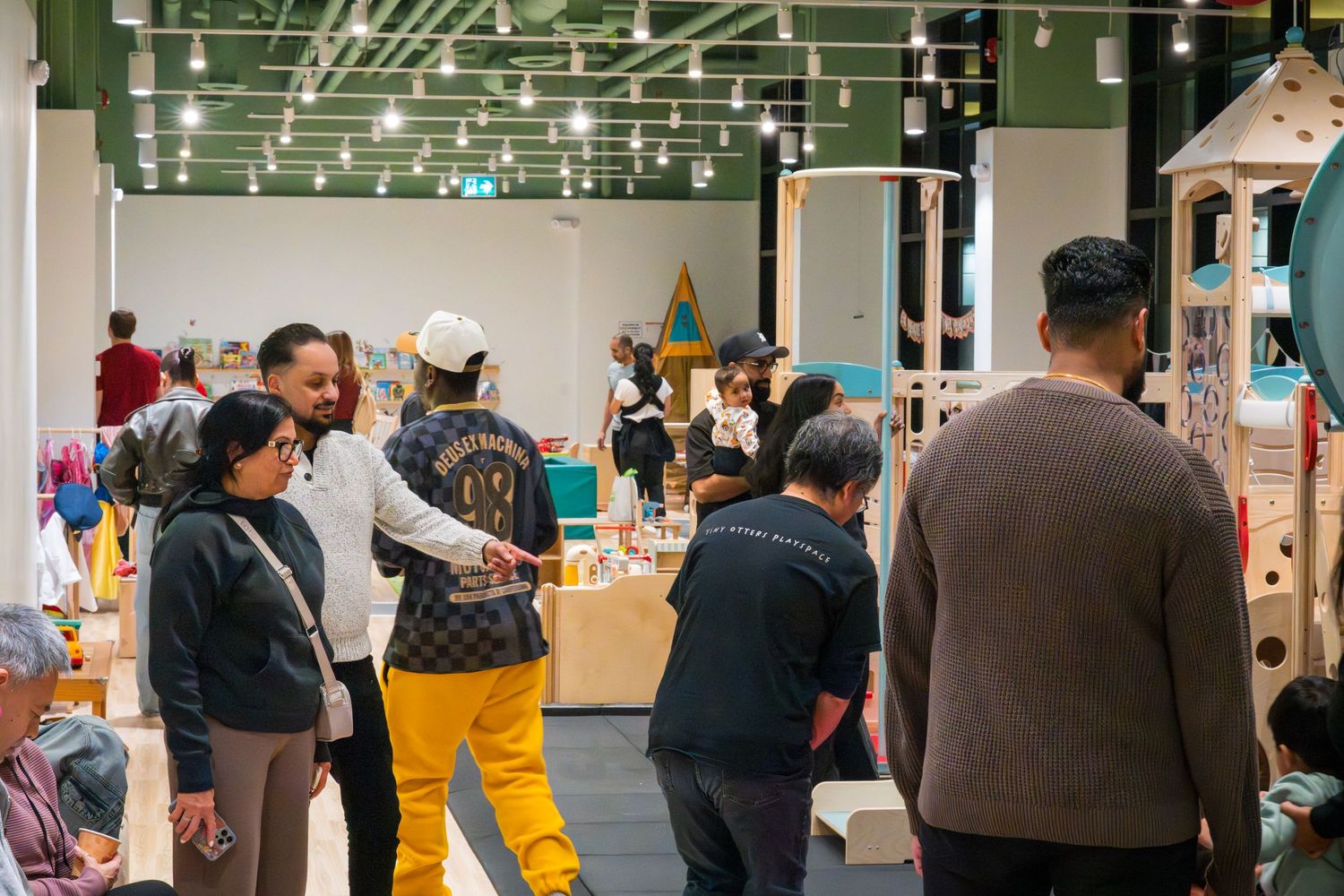 Diverse group of adults socializing and mingling in a spacious modern indoor children's play center.