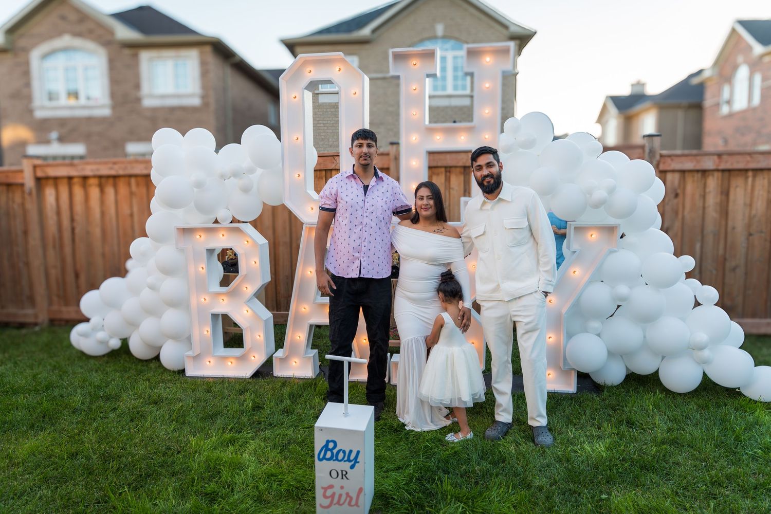 Family and friend pose at gender reveal party with OH BABY marquee sign and white balloon decor.