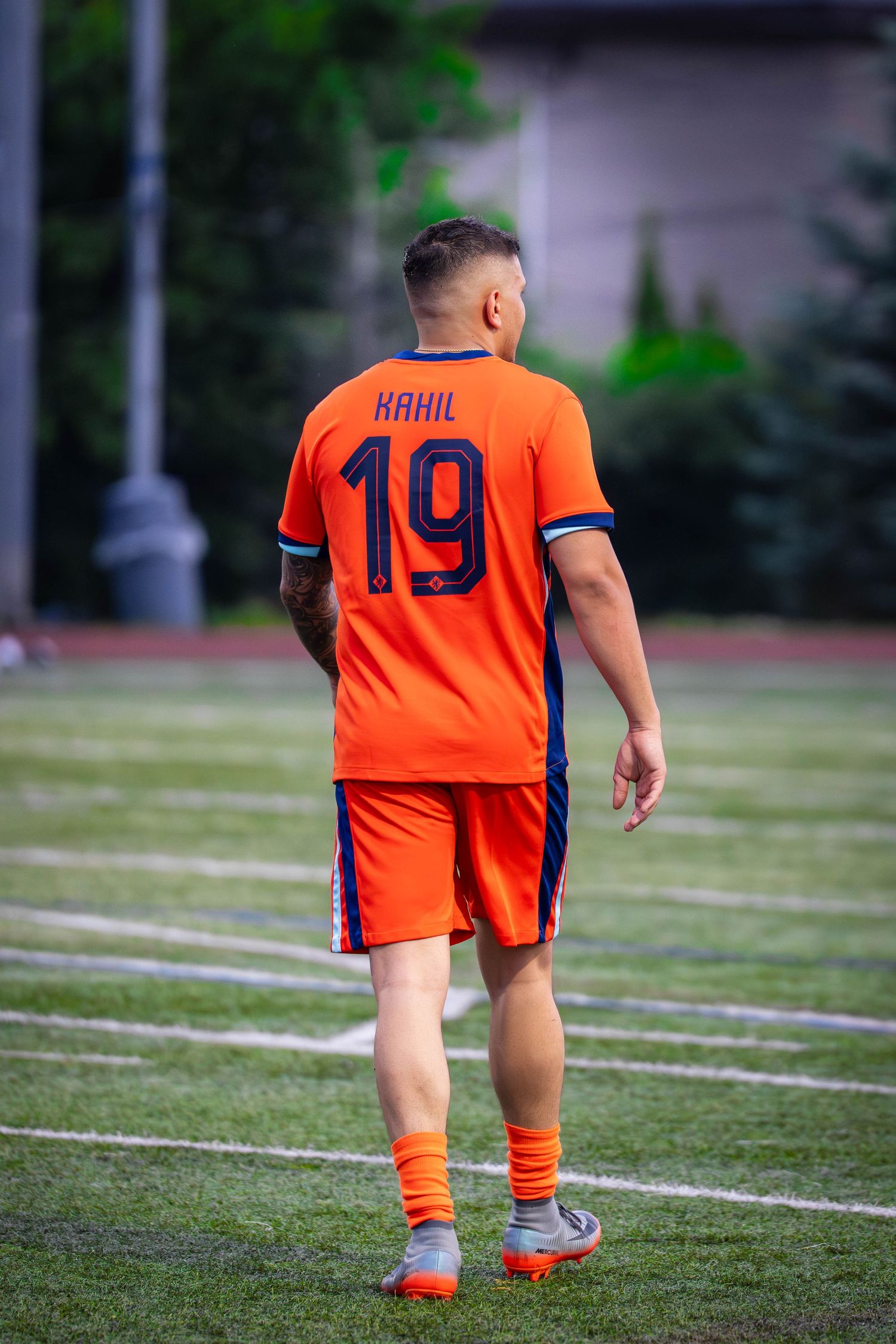 A soccer player wearing number 19 orange jersey walks on the field.