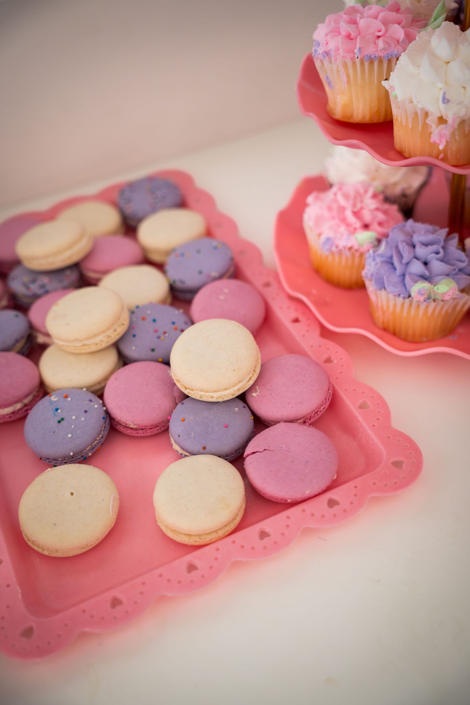 Close-up of pastel macarons and decorated cupcakes on pink serving platters.