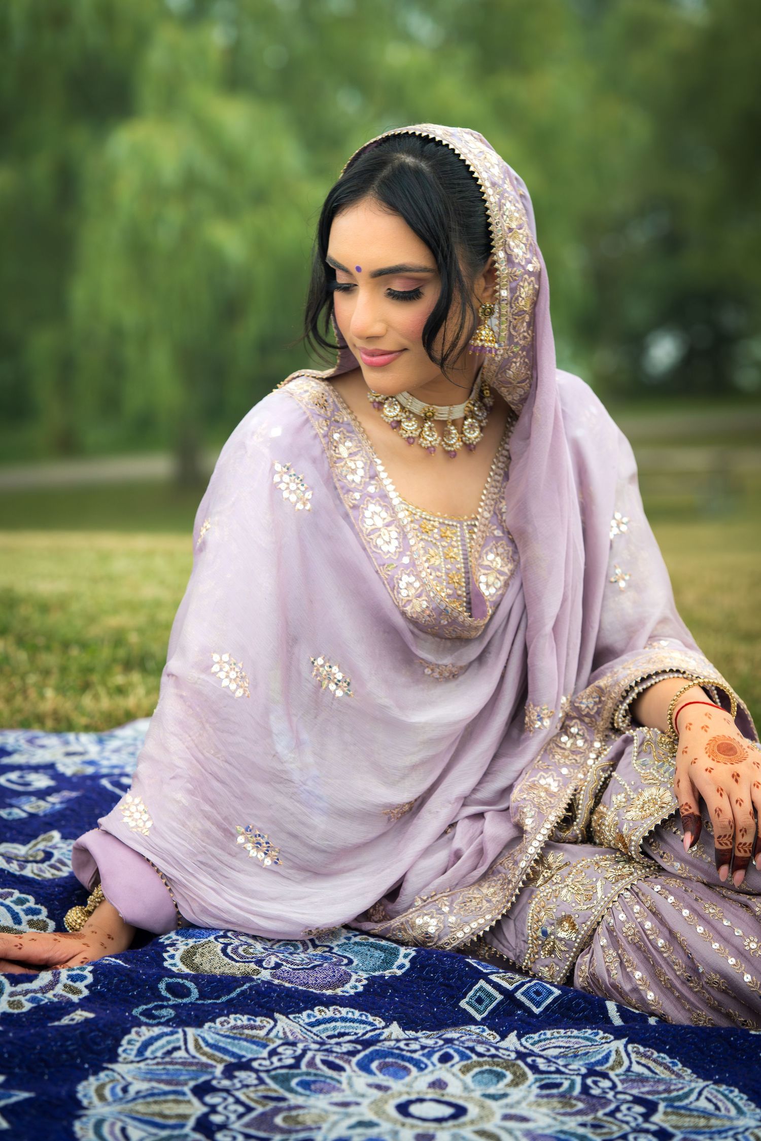 Detailed view of lavender and gold traditional dress against blue patterned textile outdoors.