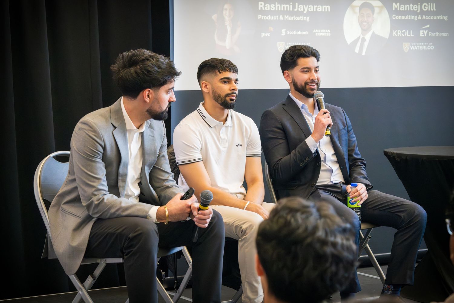 Panel discussion featuring multiple speakers seated on stage with branded backdrop.