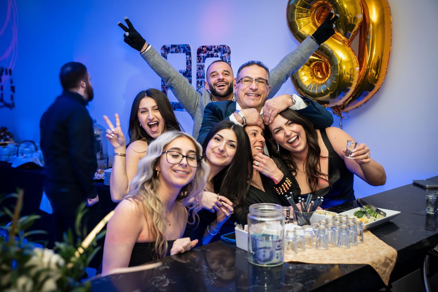 Party guests socializing at event with blue lighting and gold balloon decor.