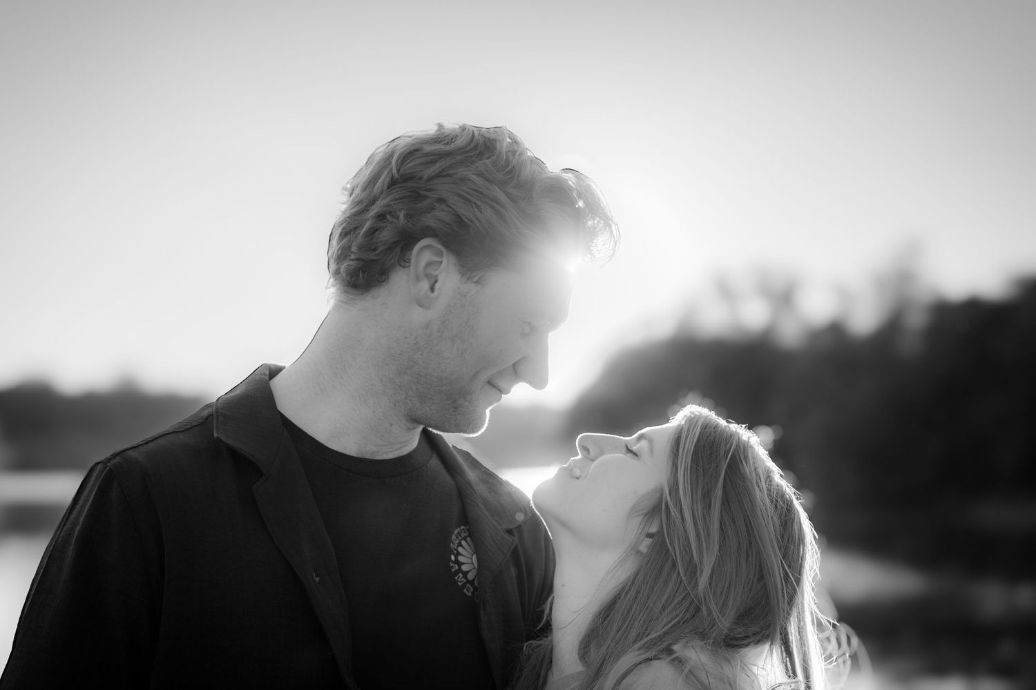 Black and white photo of a couple gazing at each other outdoors at sunset.