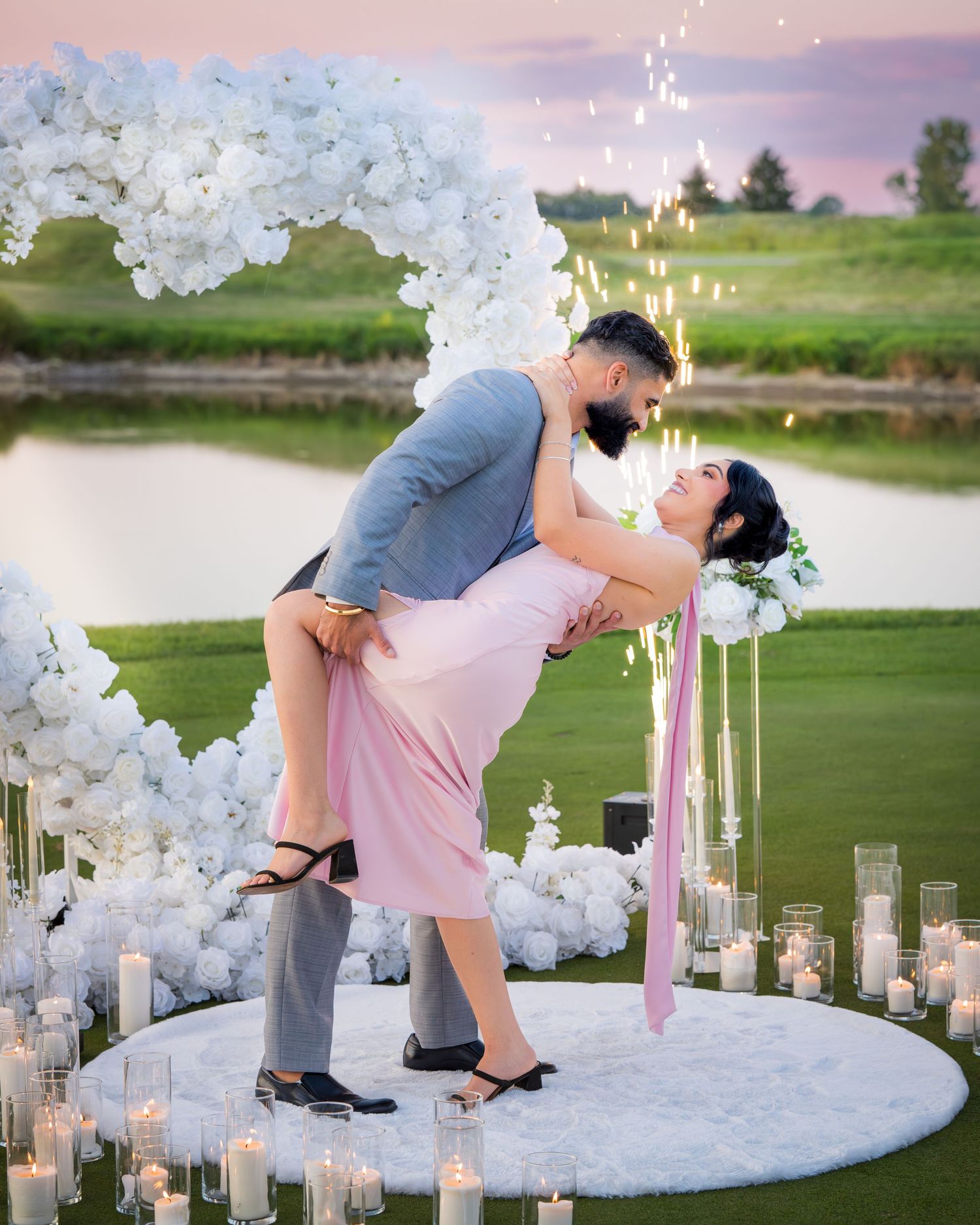 Romantic dip pose on a white circular platform surrounded by white balloon decorations at sunset.
