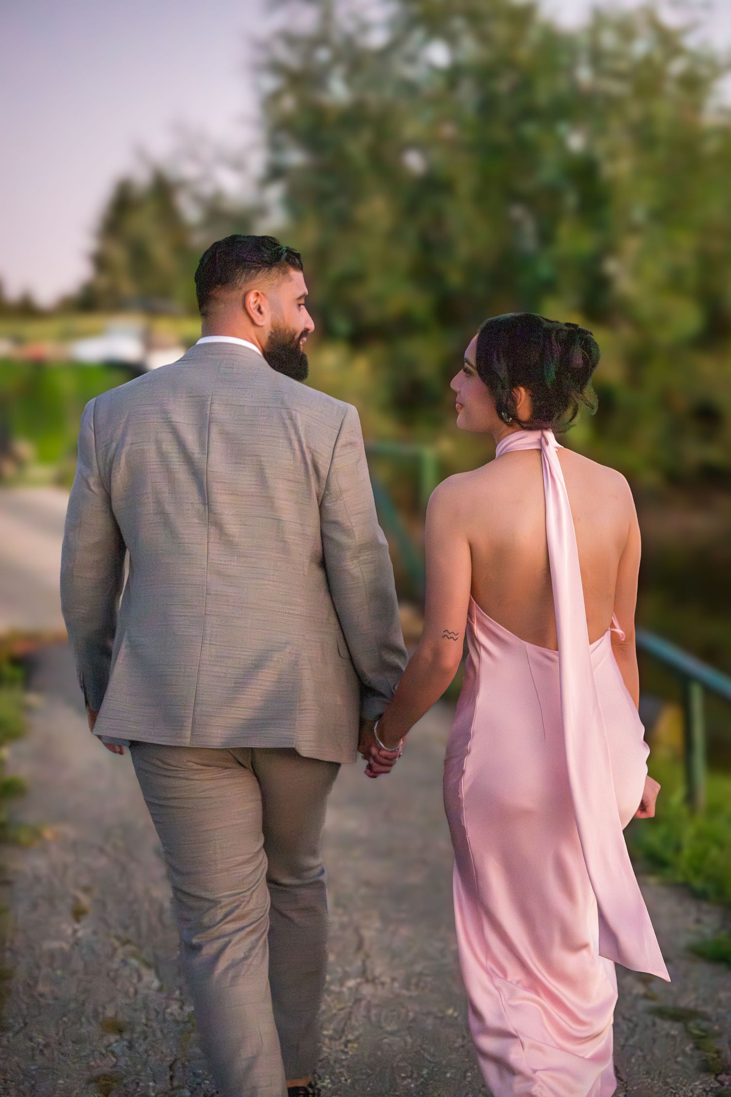 Couple in pink dress and gray suit walking together on a path during golden hour.