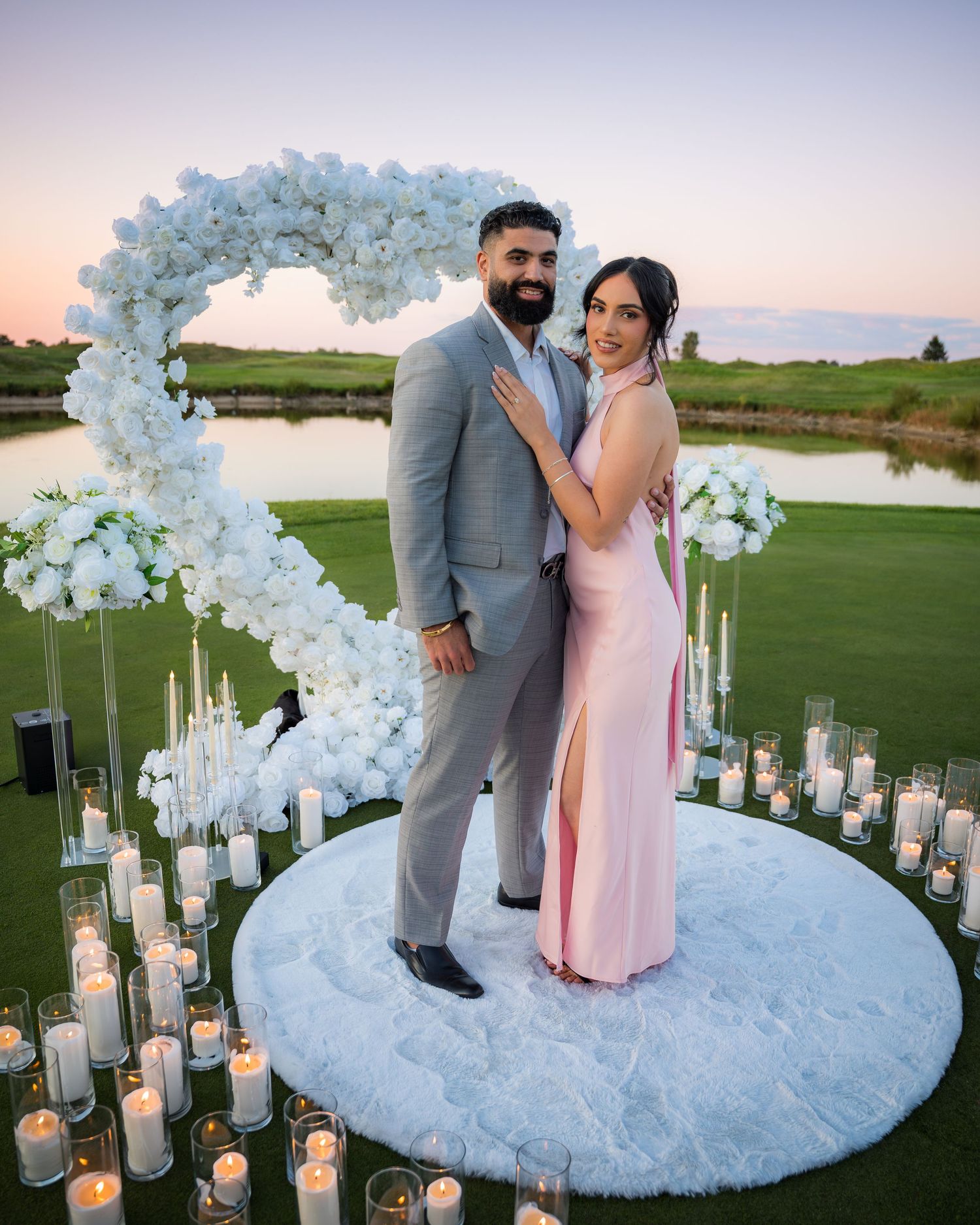 Elegant outdoor proposal scene with light blue floral arch and glowing candles at dusk.