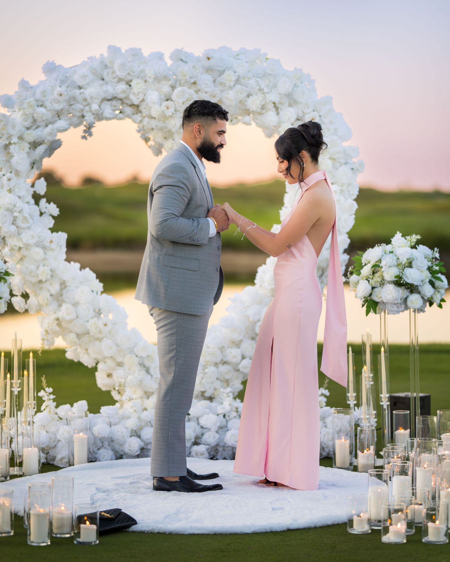 A romantic proposal setting with white floral arches and glowing candles.
