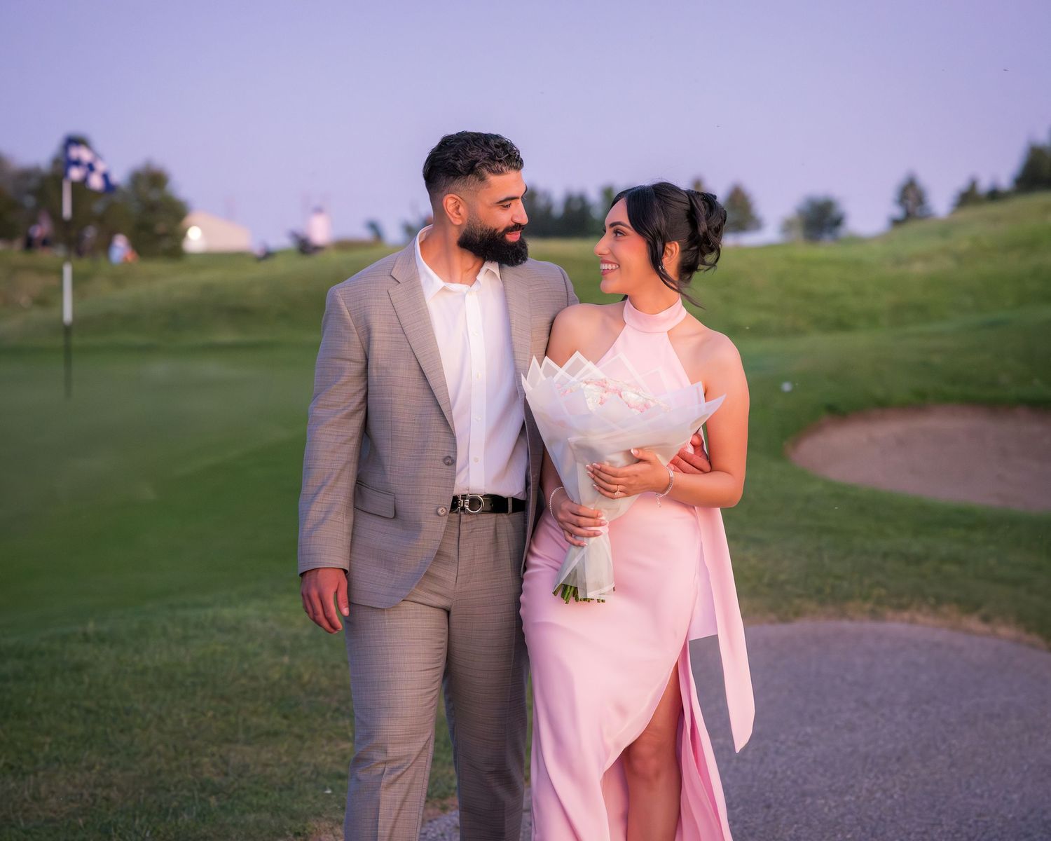 A couple in coordinated formal wear embraces while walking outdoors.