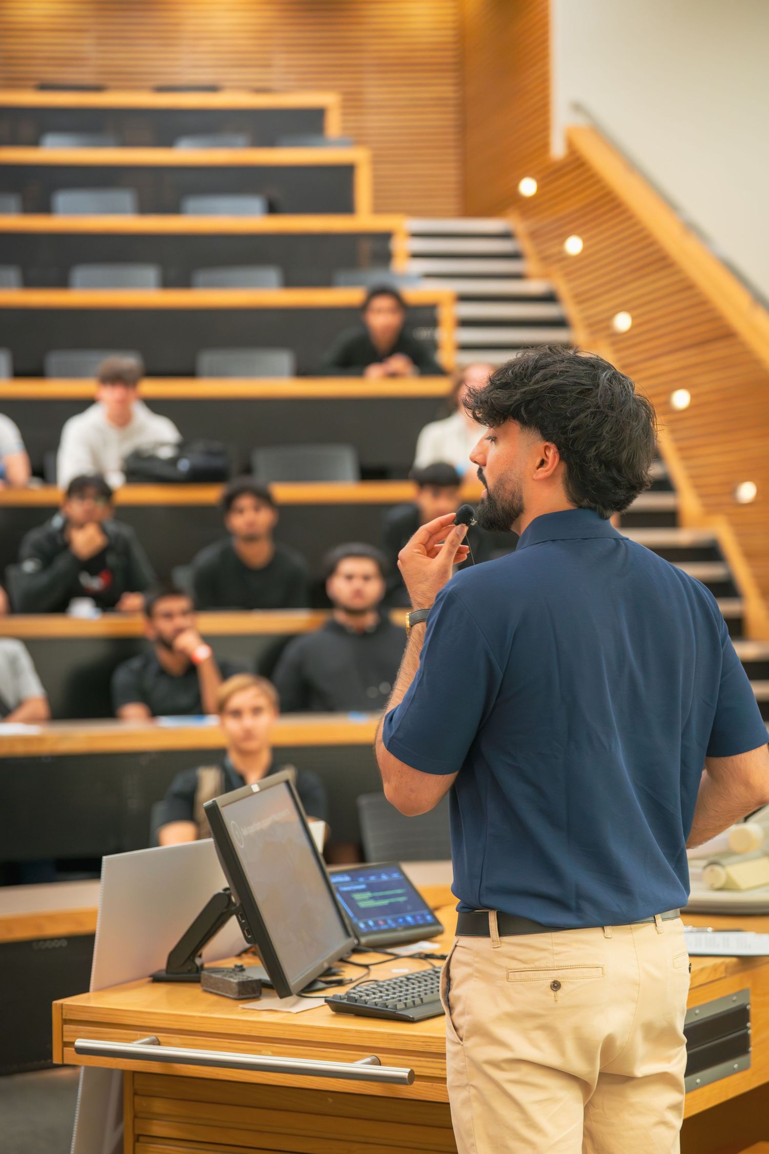 Presenters in navy polo shirts engage with audience from front of lecture hall.