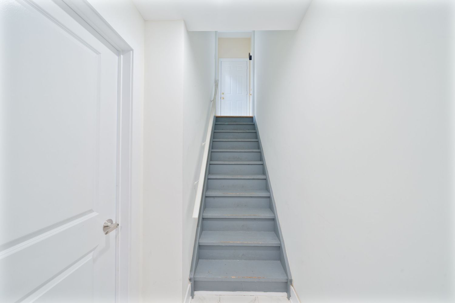 White interior hallway with wooden staircase and bright natural lighting from above.