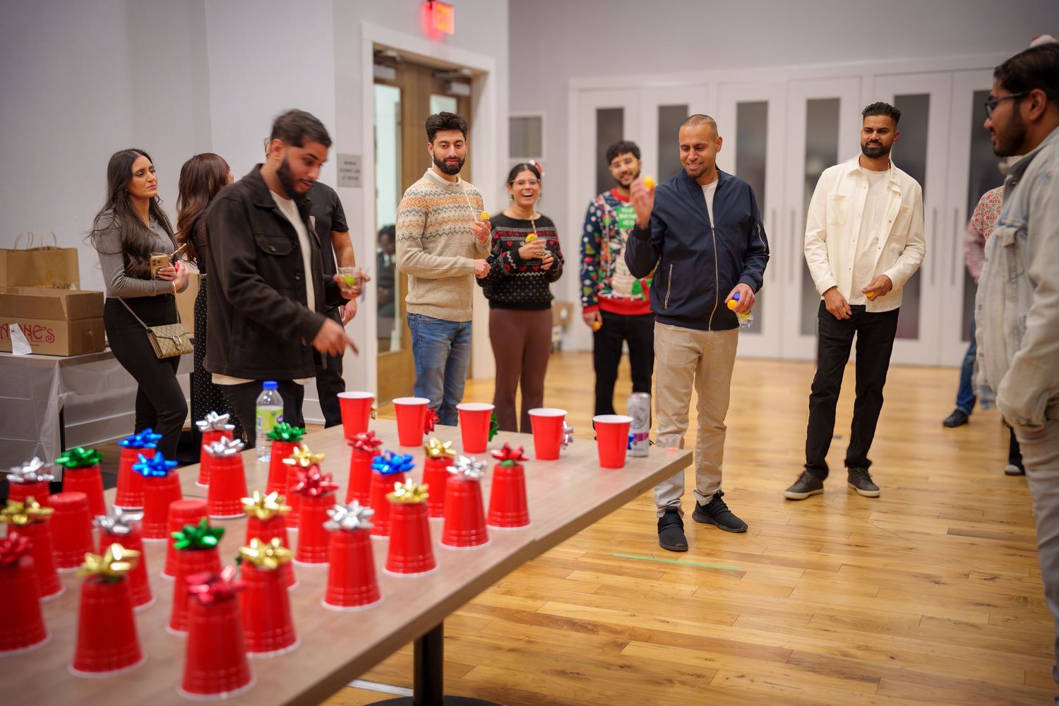 Red plastic cups arranged in rows on hardwood floor with people standing around viewing them.
