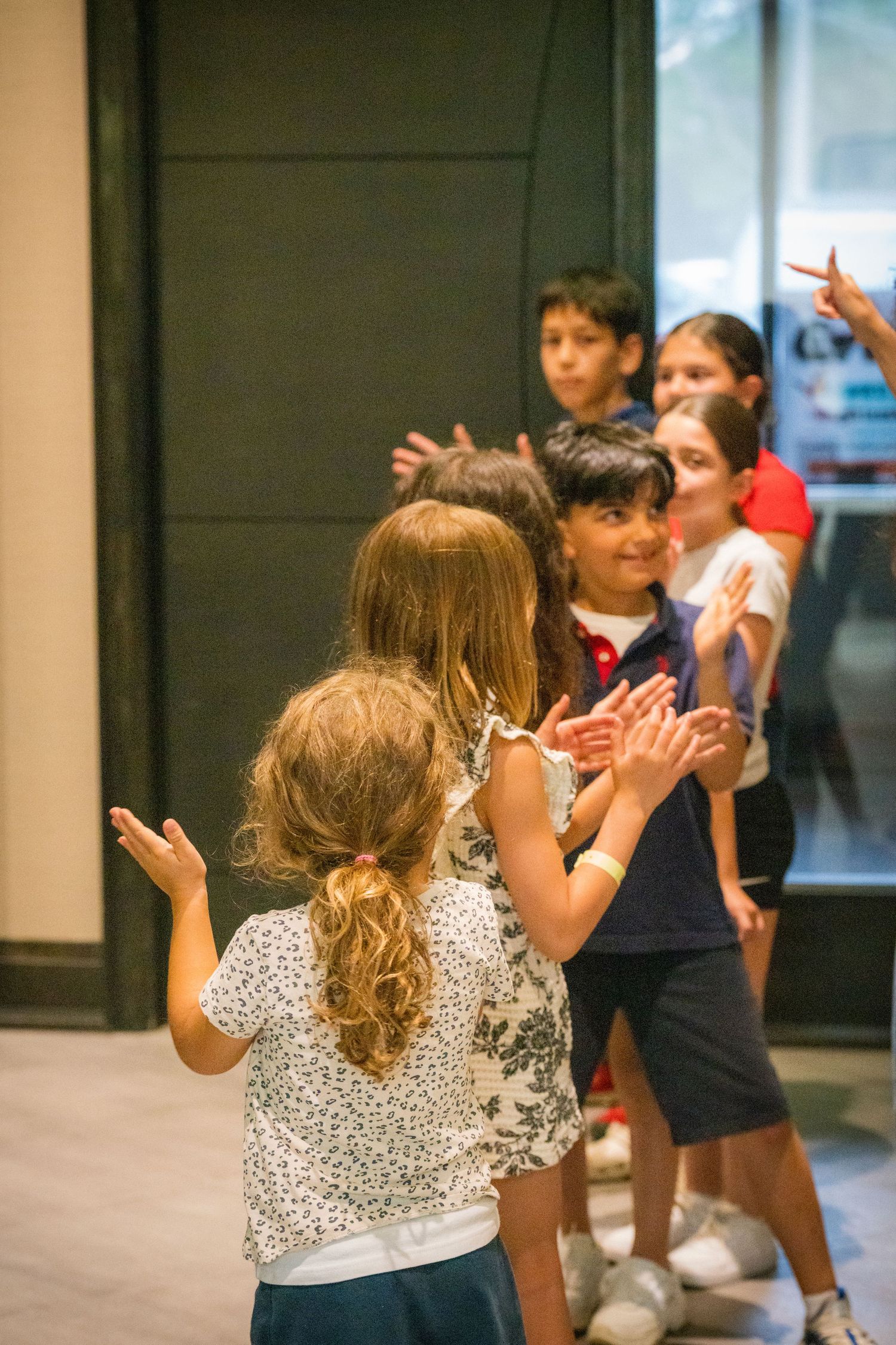 Group of children clapping and smiling during interactive activity in modern indoor space.