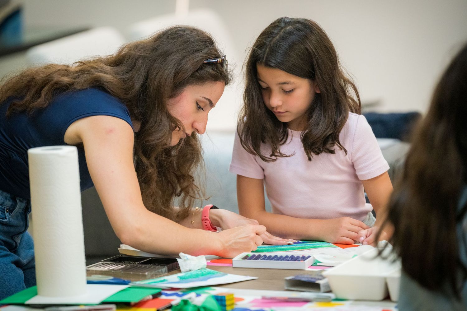 Adult woman and young girl collaborating on a colorful arts and crafts project at a table covered with paper.