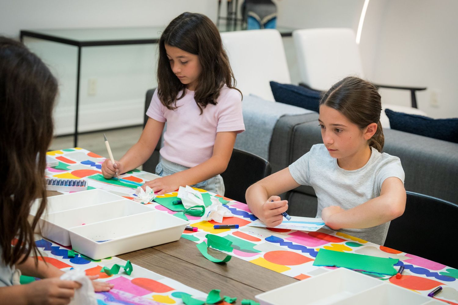 Children engage in creative paper collage activity at a colorful art workshop table.