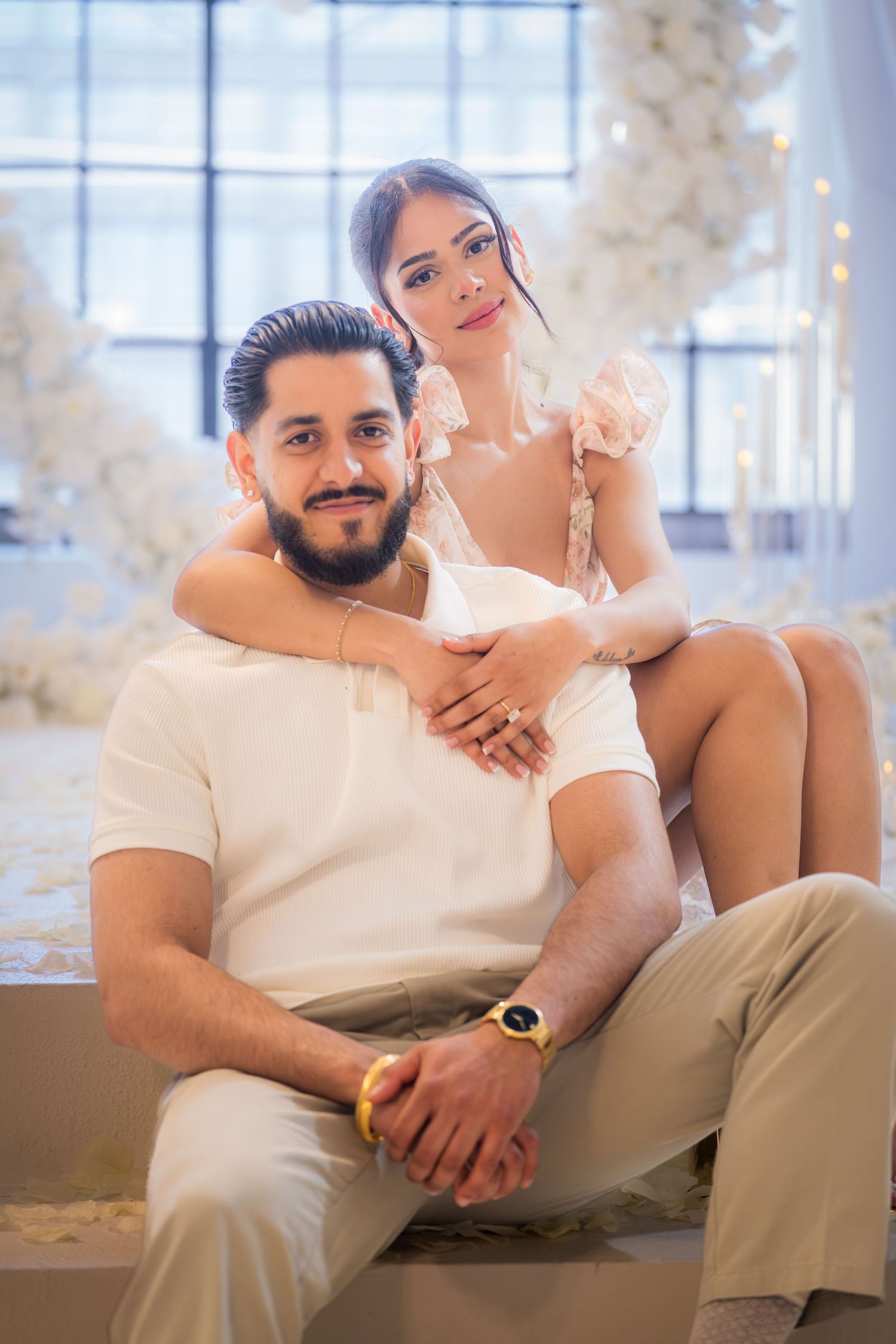 Smiling couple sitting together in a beautifully decorated white floral engagement setting.