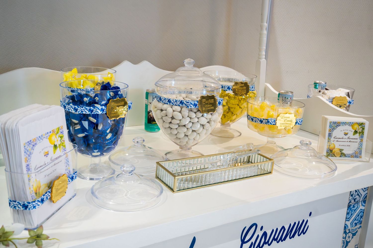 Elegant candy buffet table with blue and yellow decor, glass jars filled with sweets, and Giovanni branding.