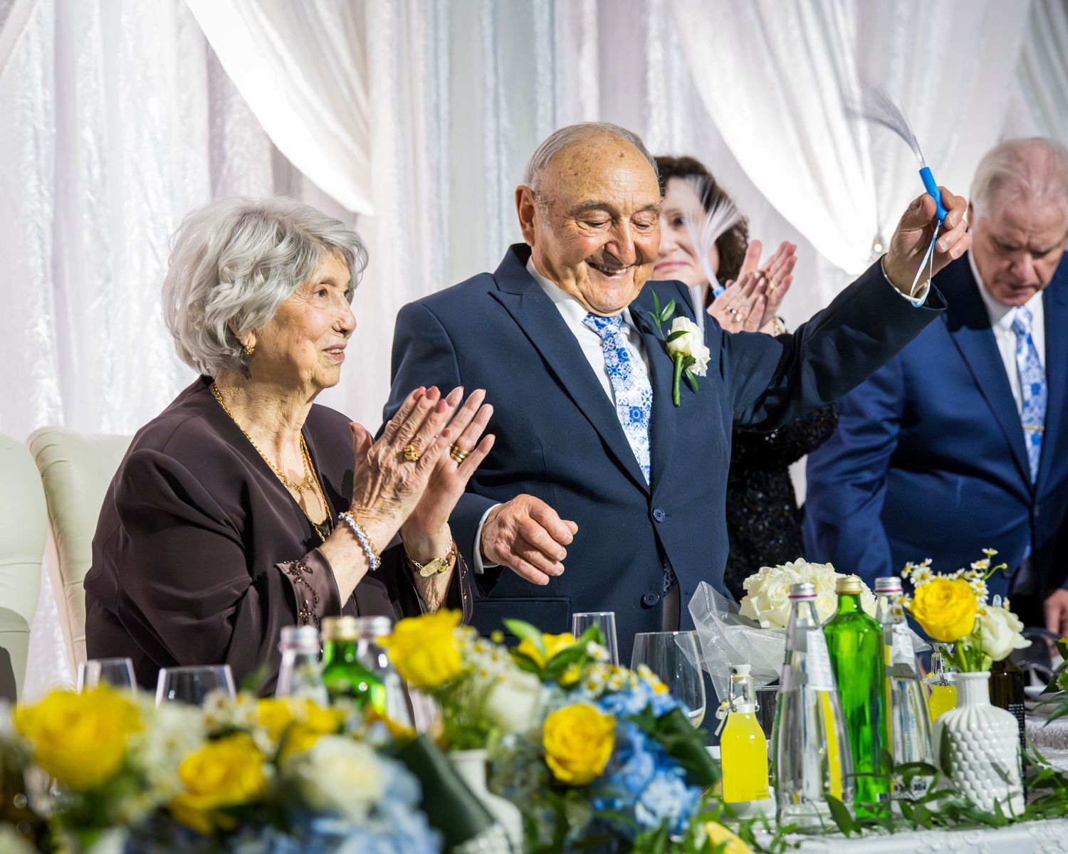 Elderly couple celebrating anniversary as guests raise glasses for a champagne toast.