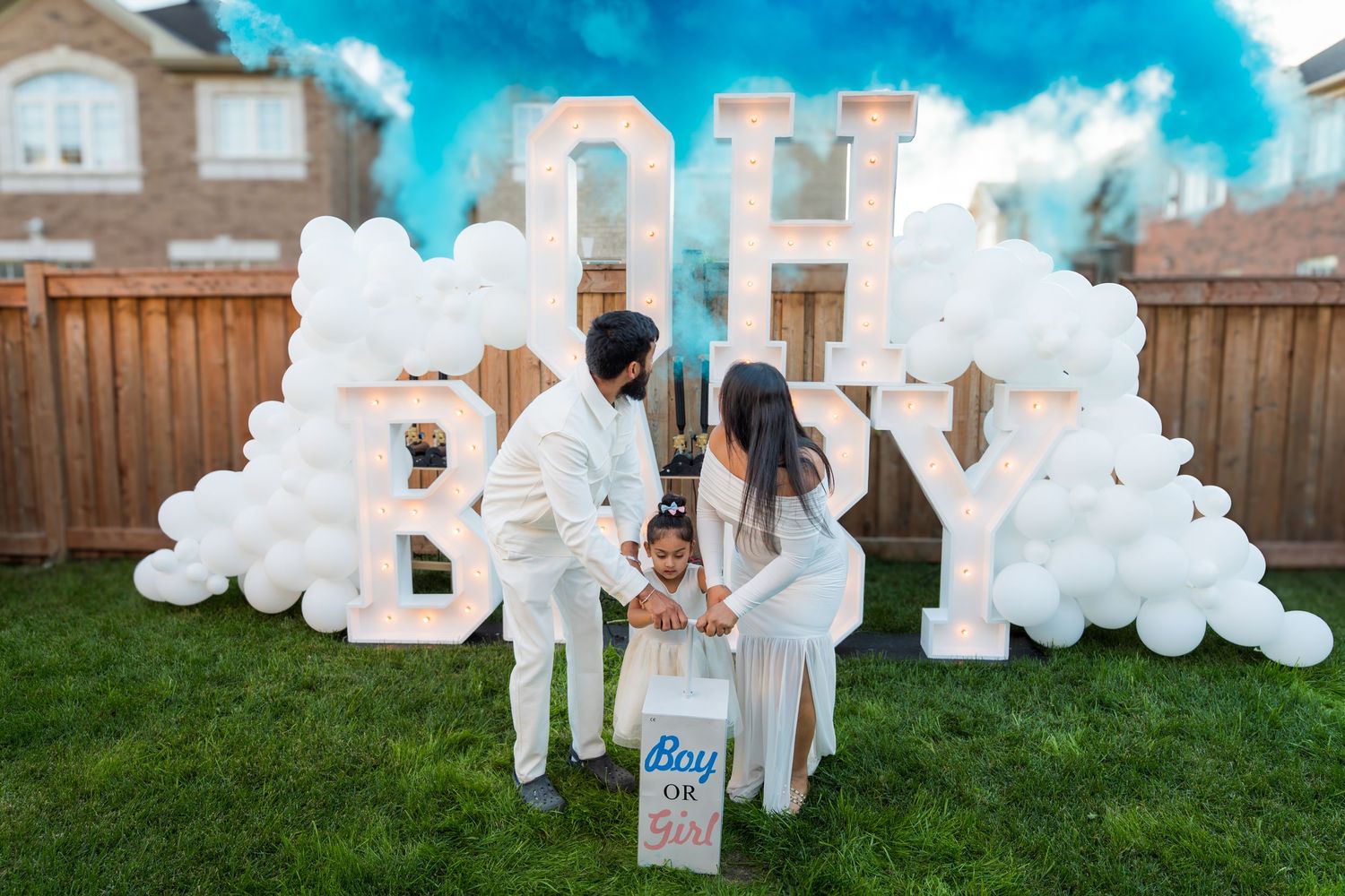 Family opening gender reveal box releasing blue smoke in front of OH BABY balloon display.