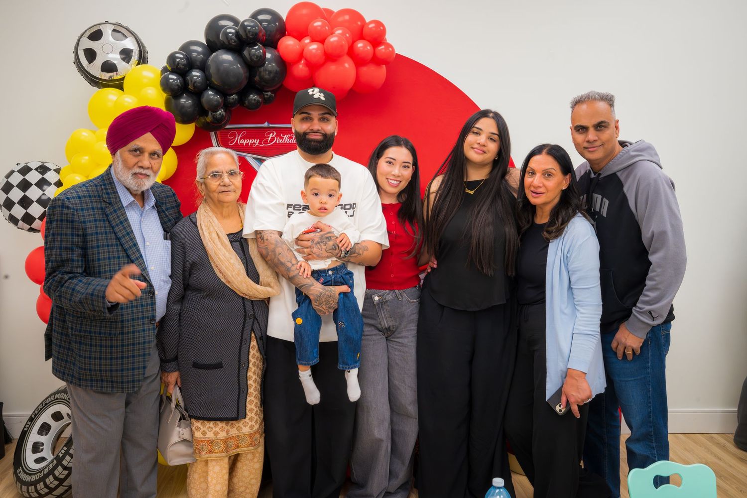 Family group photo at a racing-themed birthday party with colorful balloons and decorations.