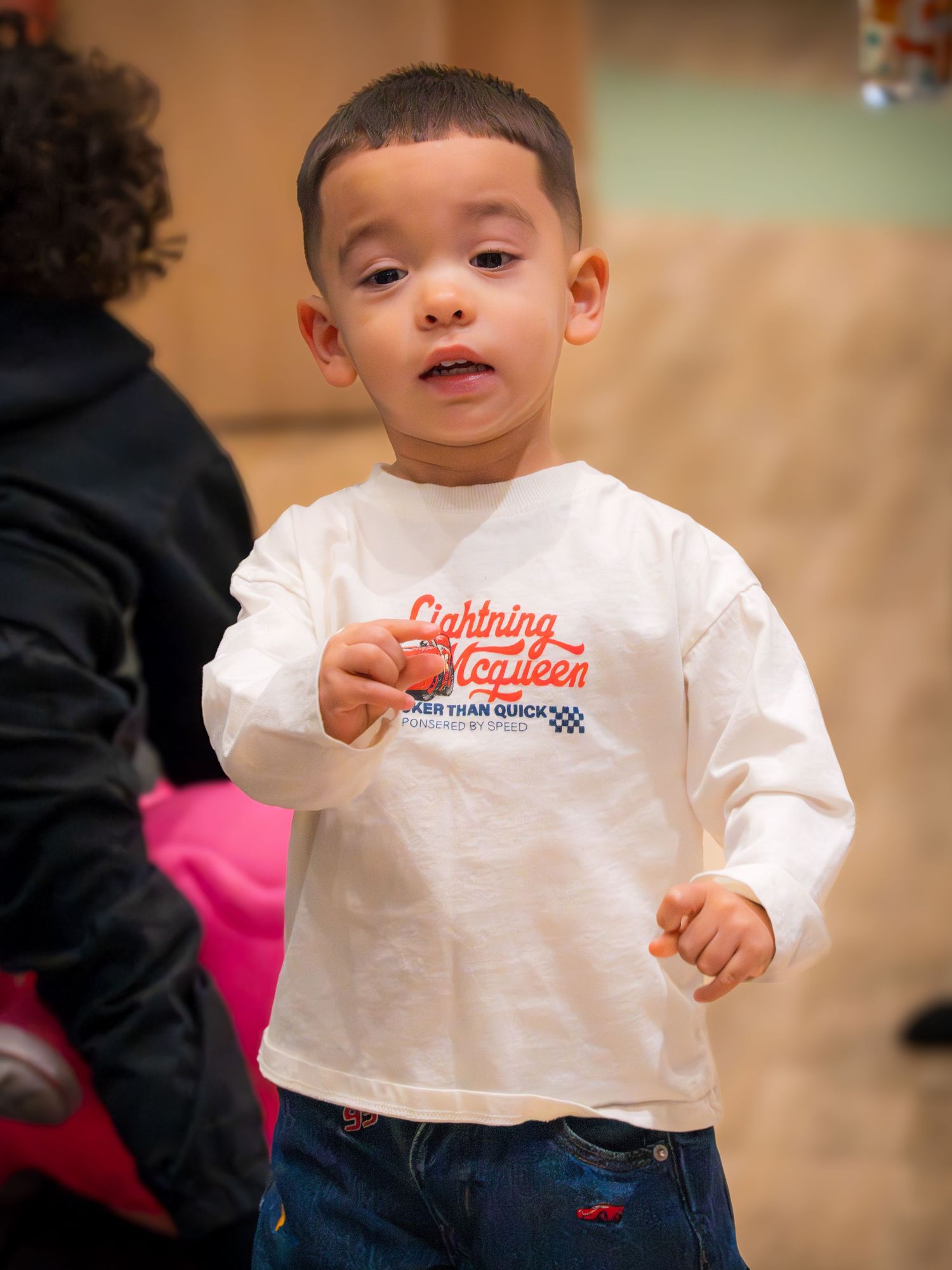 A toddler in a Lightning McQueen shirt stands and looks around during an indoor play event.