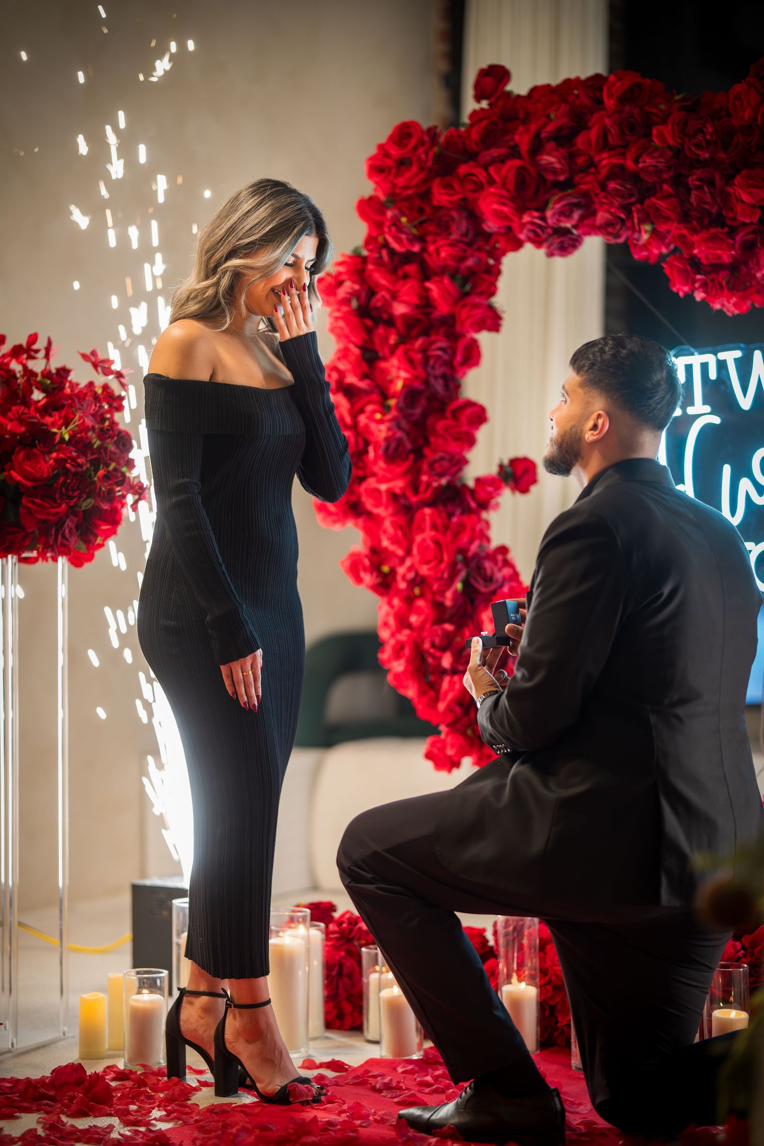 Proposal scene with sparklers, red roses, and neon lighting creating romantic atmosphere.
