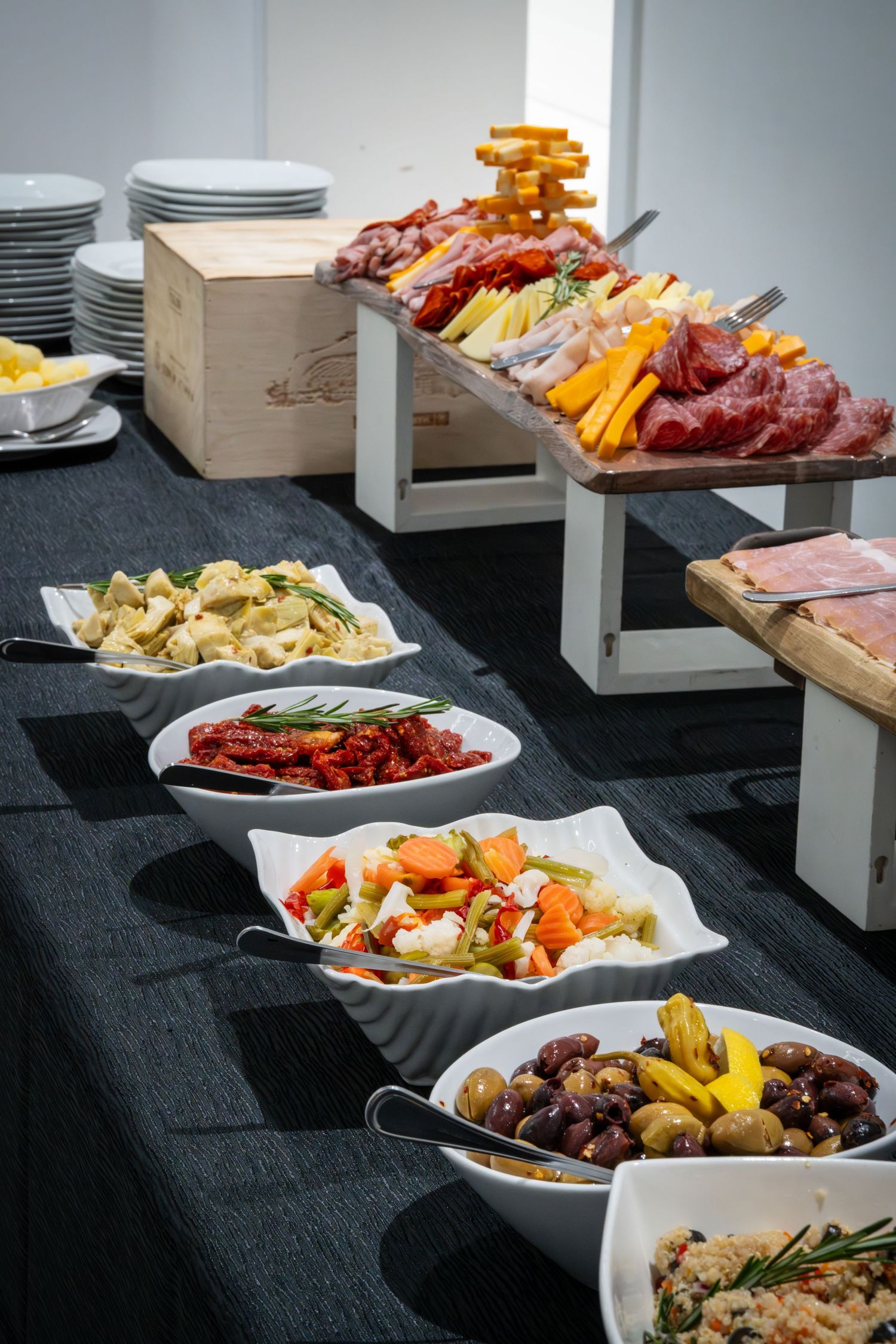 Catering buffet setup with various appetizers and meats displayed on white plates and wooden boards.