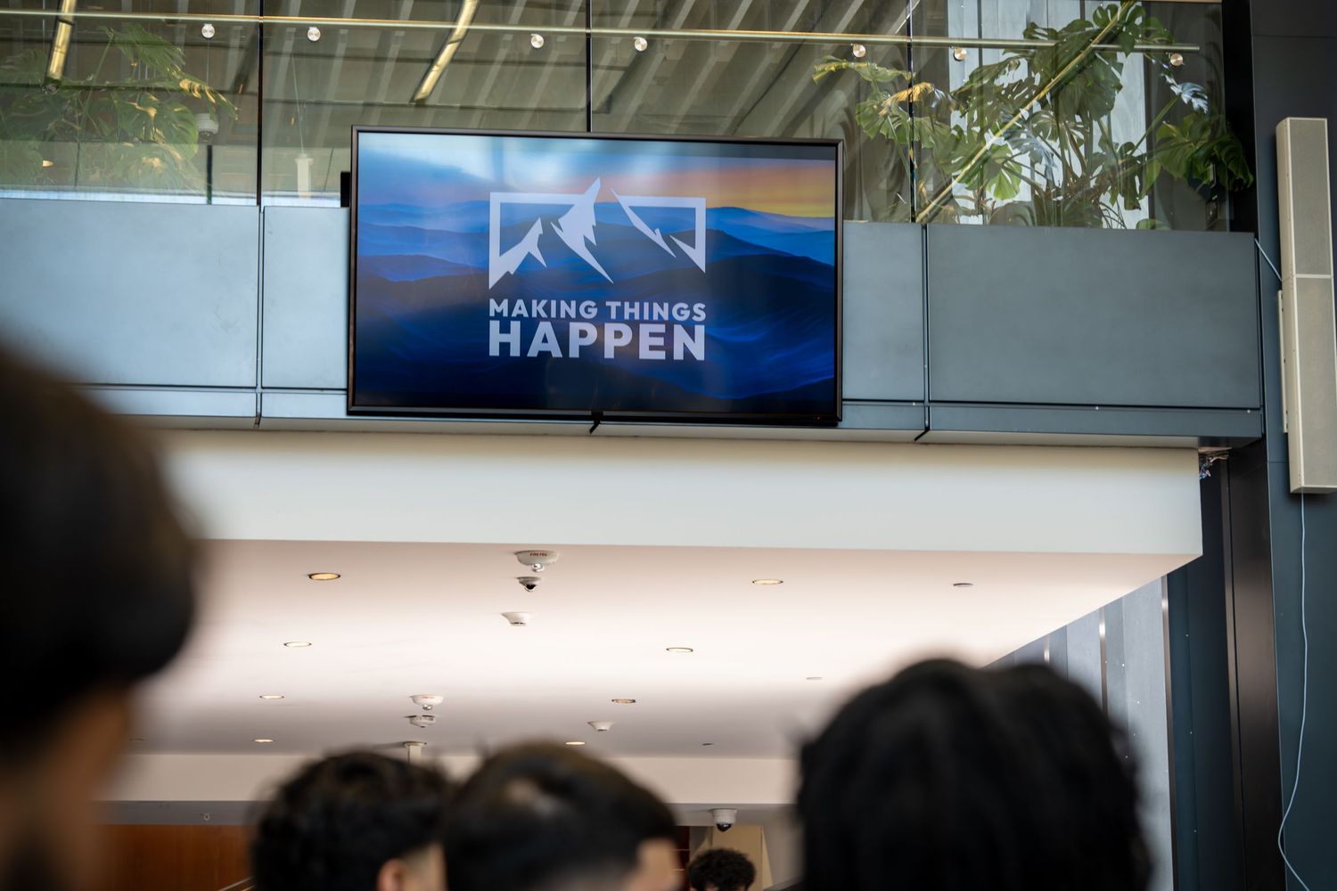 Conference venue interior with modern digital displays and lighting visible above stage area.