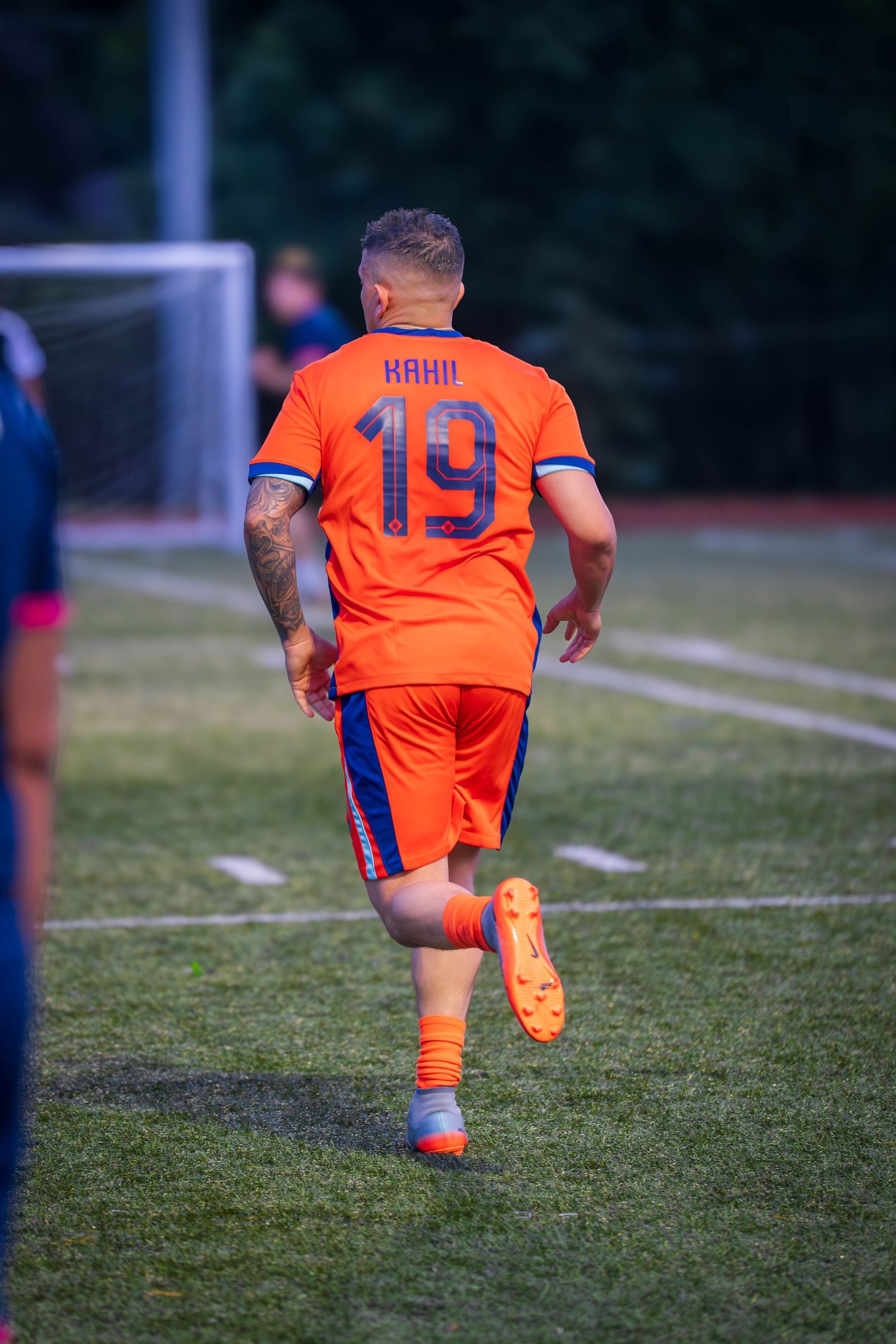 Back view of soccer player in orange uniform with number 19 and name Kaan running on field.