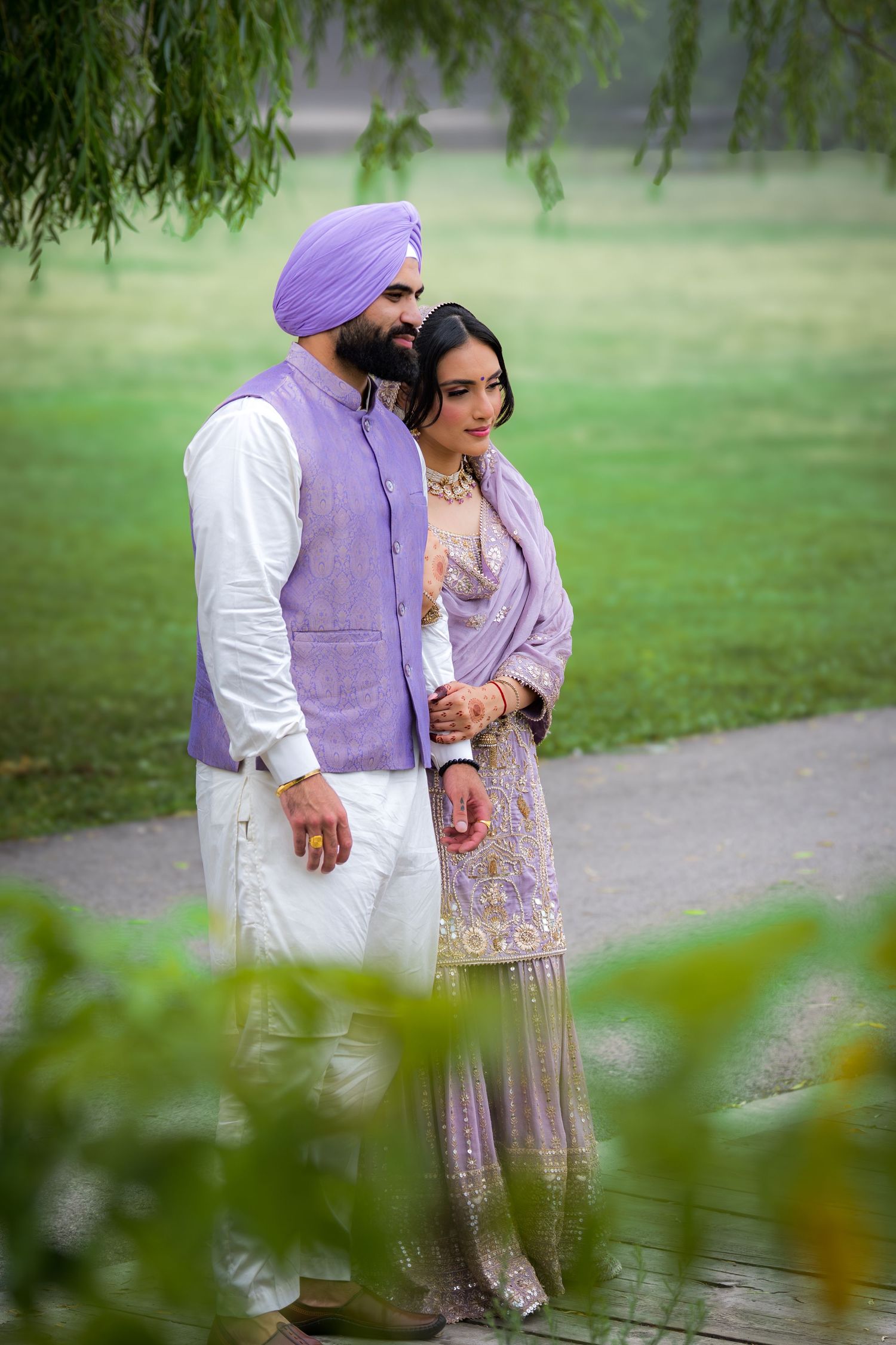 Couple in coordinated purple and white outfits walking together in a lush garden setting.