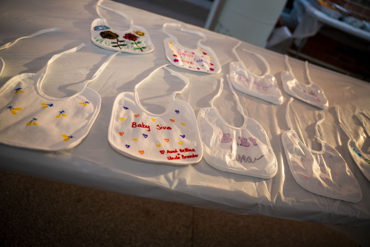 Row of decorated white baby bibs with colorful designs laid out on dark flooring.
