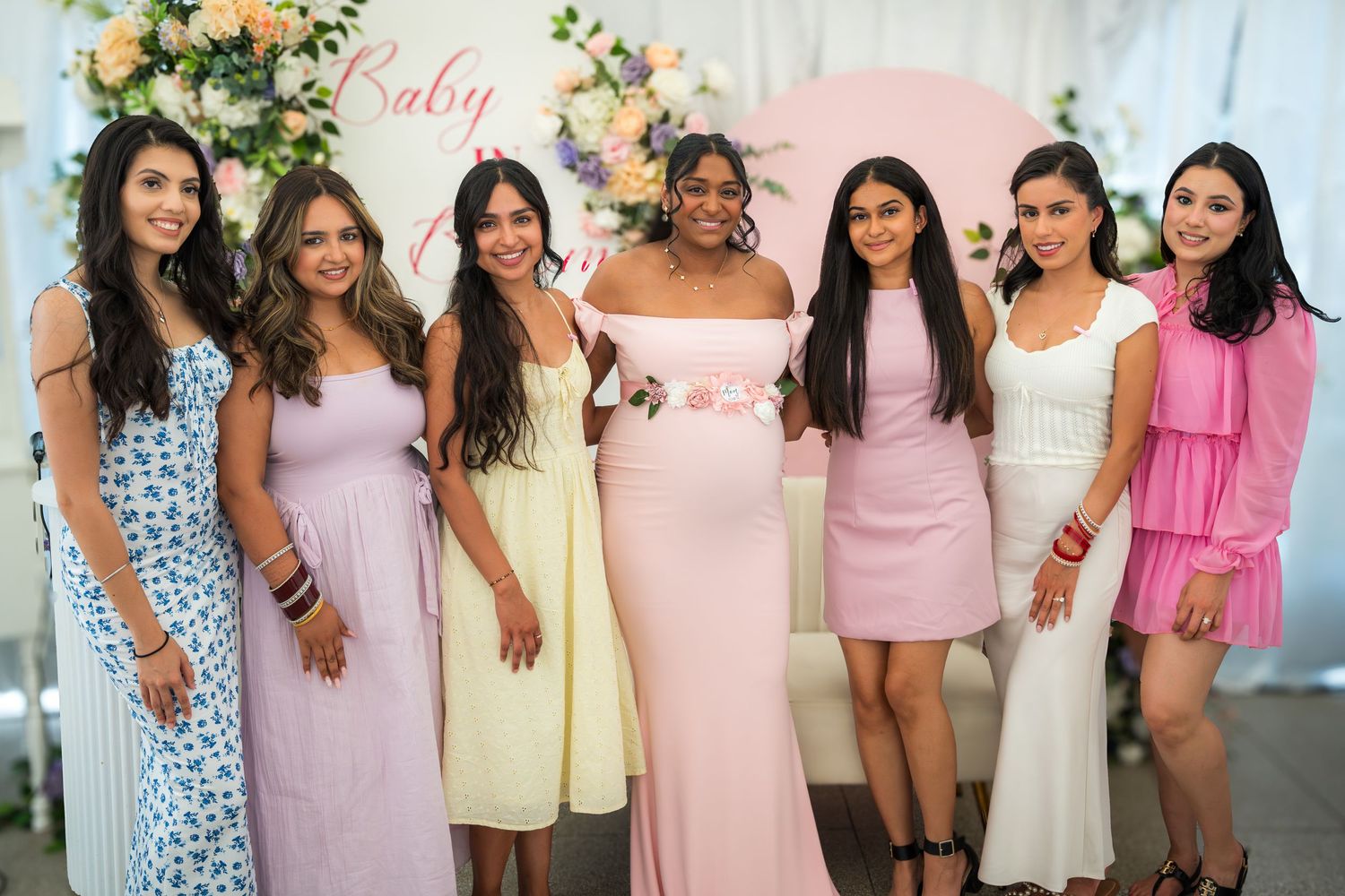 Group photo of baby shower attendees in coordinated pink and pastel outfits.