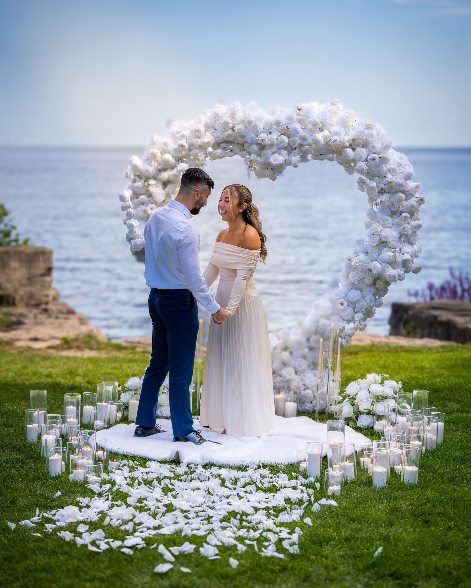 Romantic waterfront ceremony setup with white balloon arch and scattered petals.