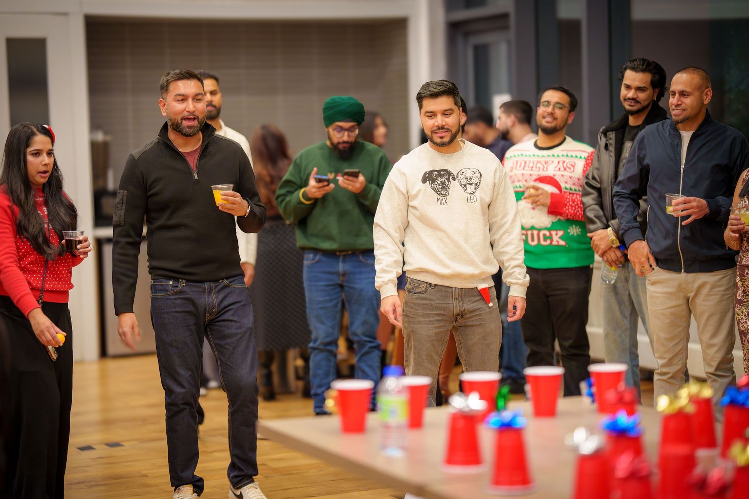 Large group of party guests watching a game involving red plastic cups.