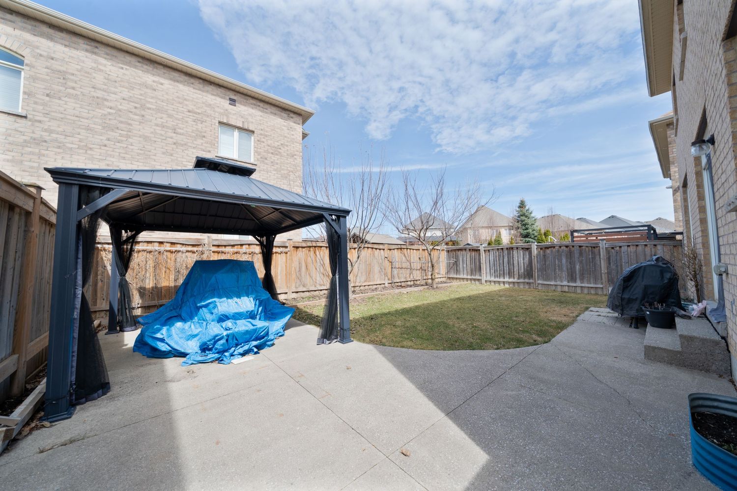 A panoramic view of a residential backyard with a wooden fence and blue tarp covering items in the corner.