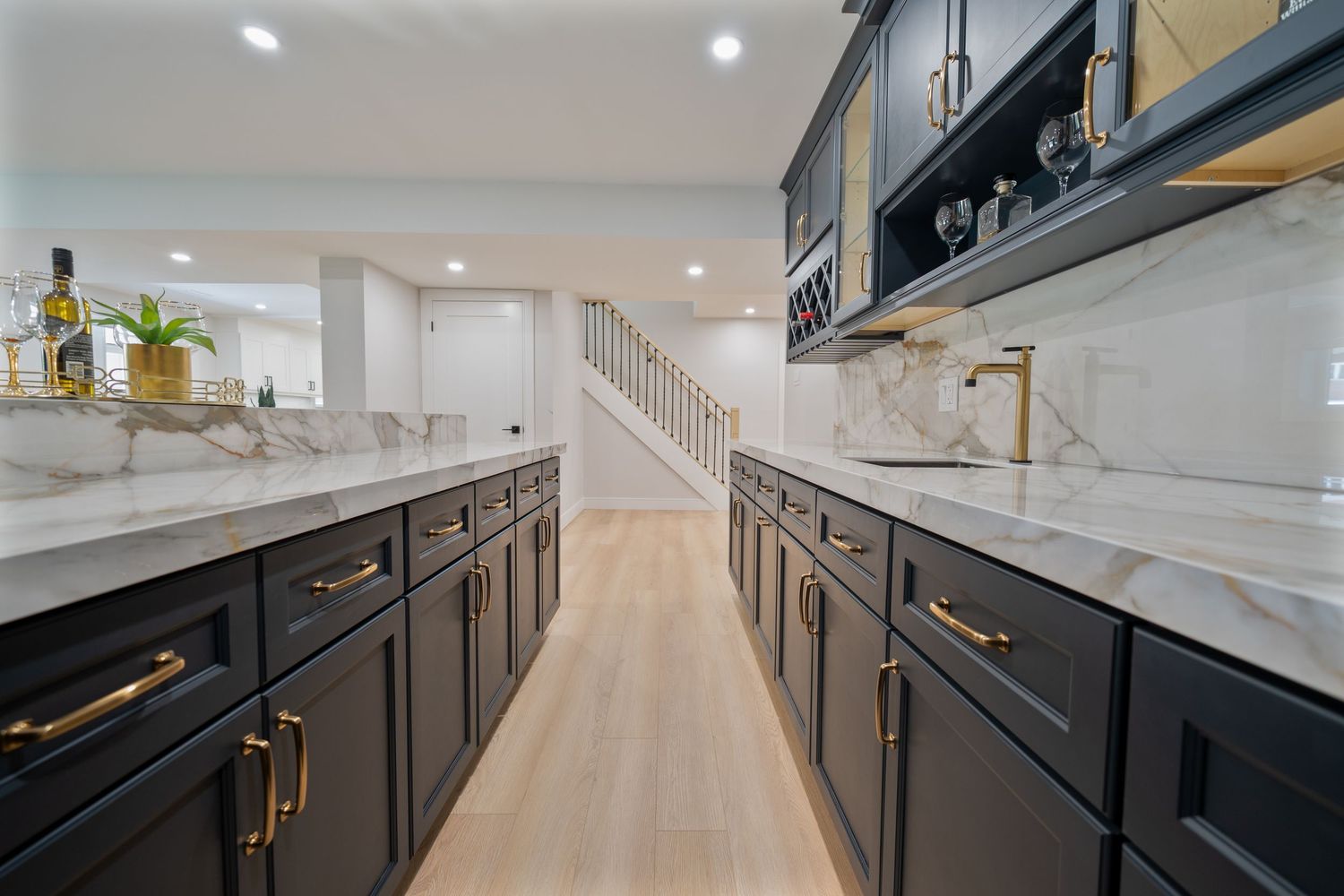 Modern kitchen design featuring dark cabinets, white marble countertops, and brass hardware with open concept layout.