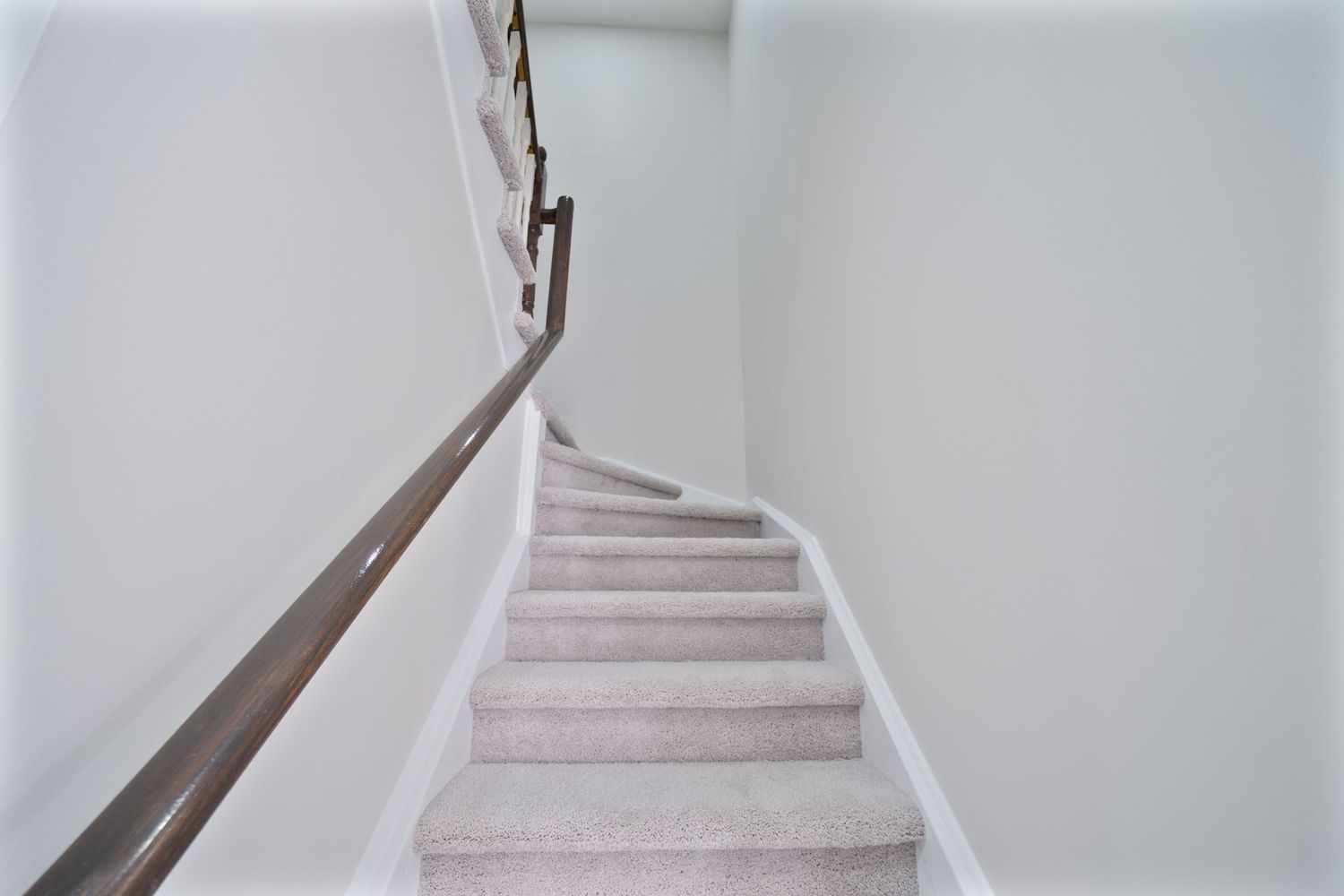 Modern white staircase with dark wood handrail curves upward in a minimalist interior design.